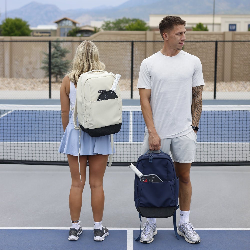 Pickleball backpacks by FORWRD in light beige and navy, with dark bottoms and pickleball paddles, on a court.
