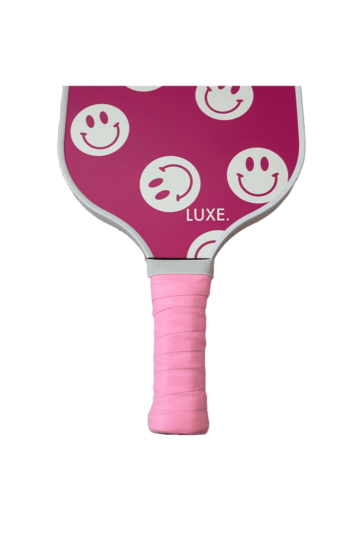 Pink pickleball paddle with smiley face graphics.