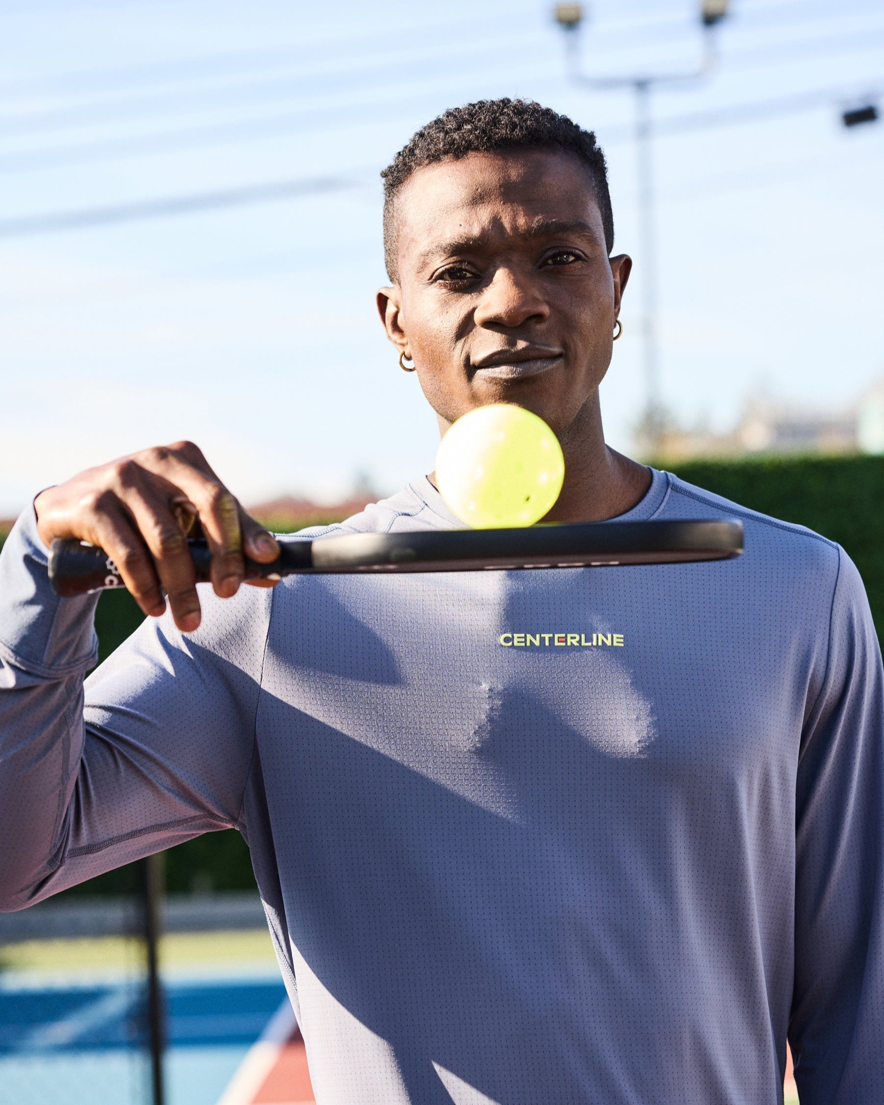Man holding pickleball paddle with ball, wearing gray long-sleeve athletic shirt.