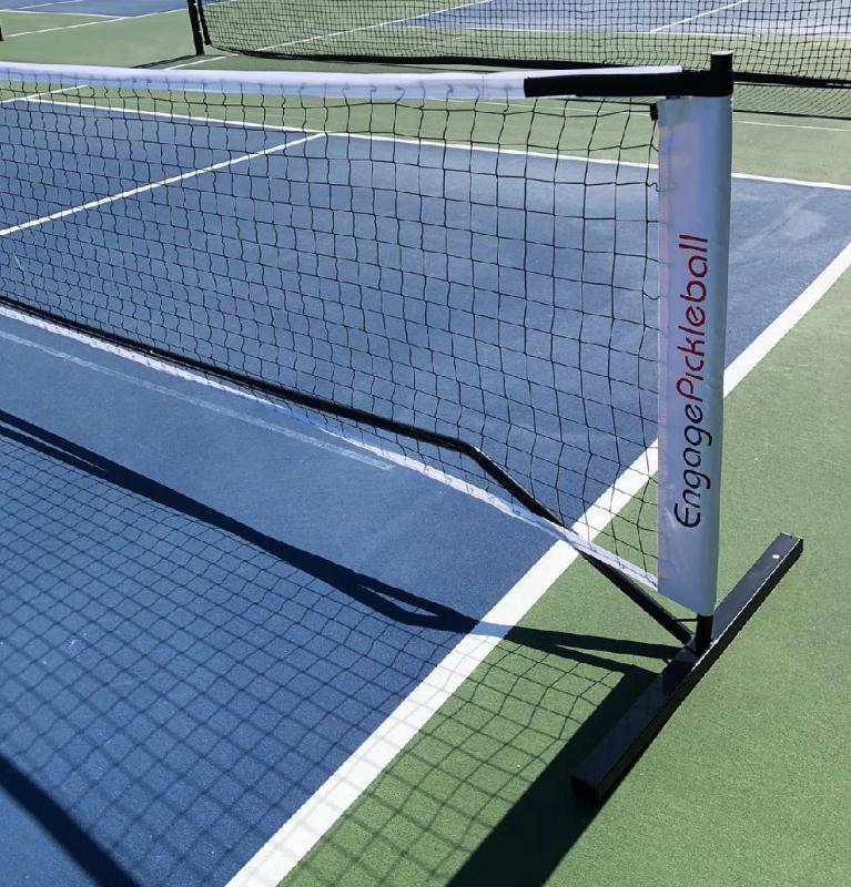 Black portable pickleball net system by EngagePickleball, featuring a white net tape and a silver-toned post, on a blue and green court.