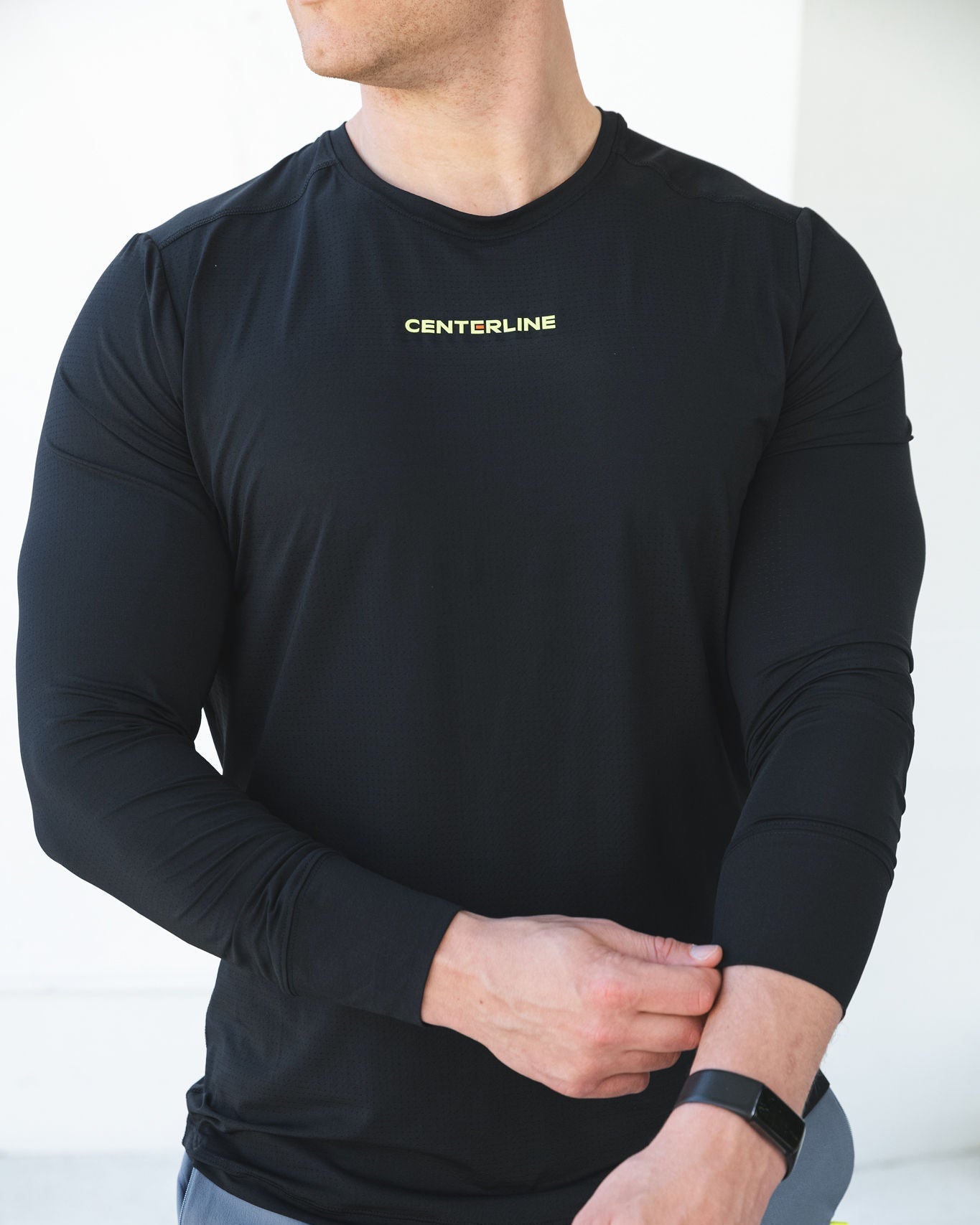 Man in a black long-sleeve shirt with "CENTERLINE" printed on the chest, adjusting his sleeve, wearing a smartwatch.