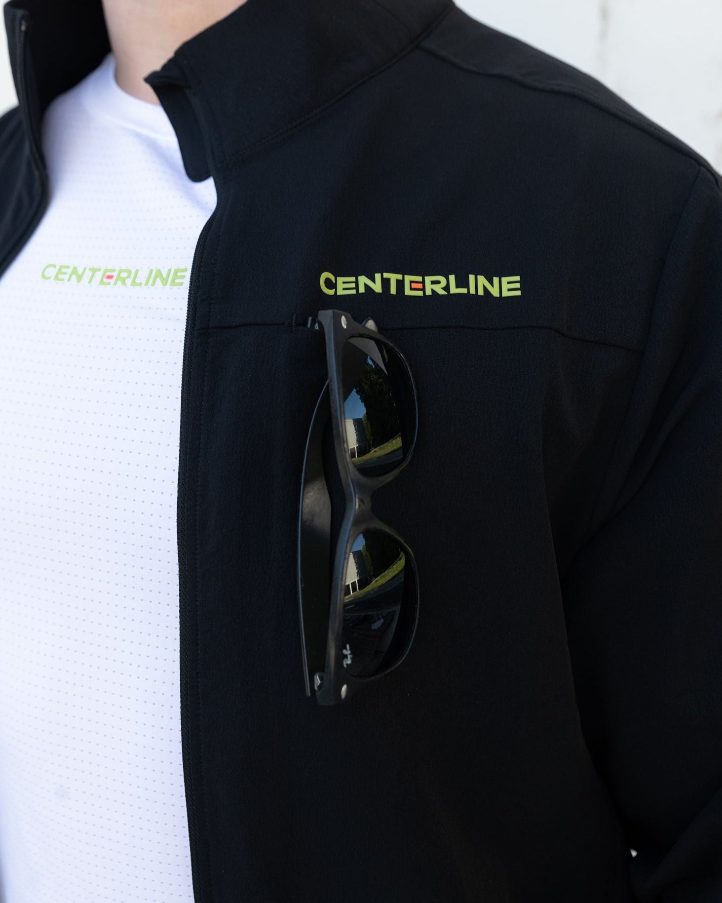 Person wearing a black jacket with the word "CENTERLINE" in yellow-green, and sunglasses in the pocket.