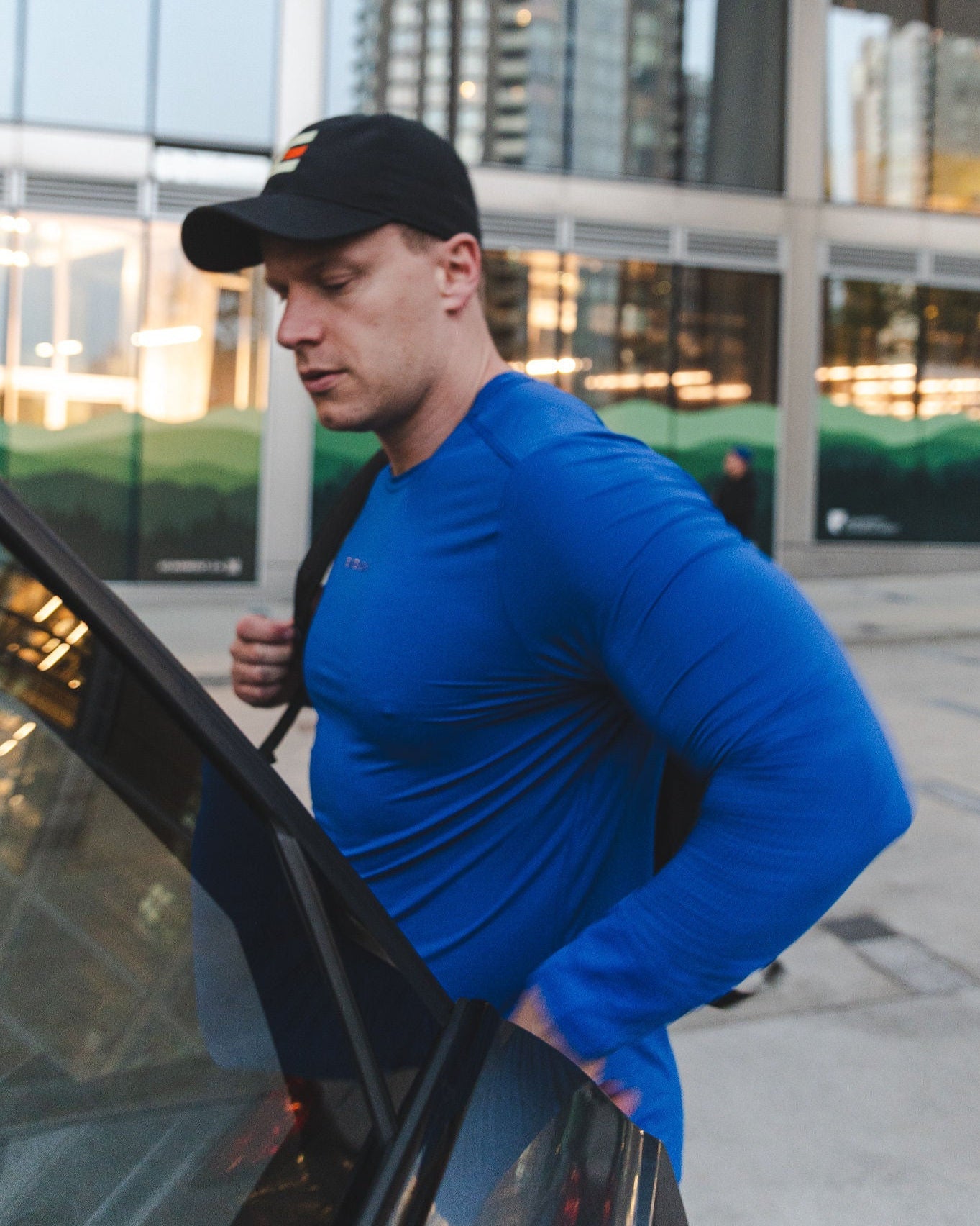 A man in a blue shirt and black baseball cap exiting a car.