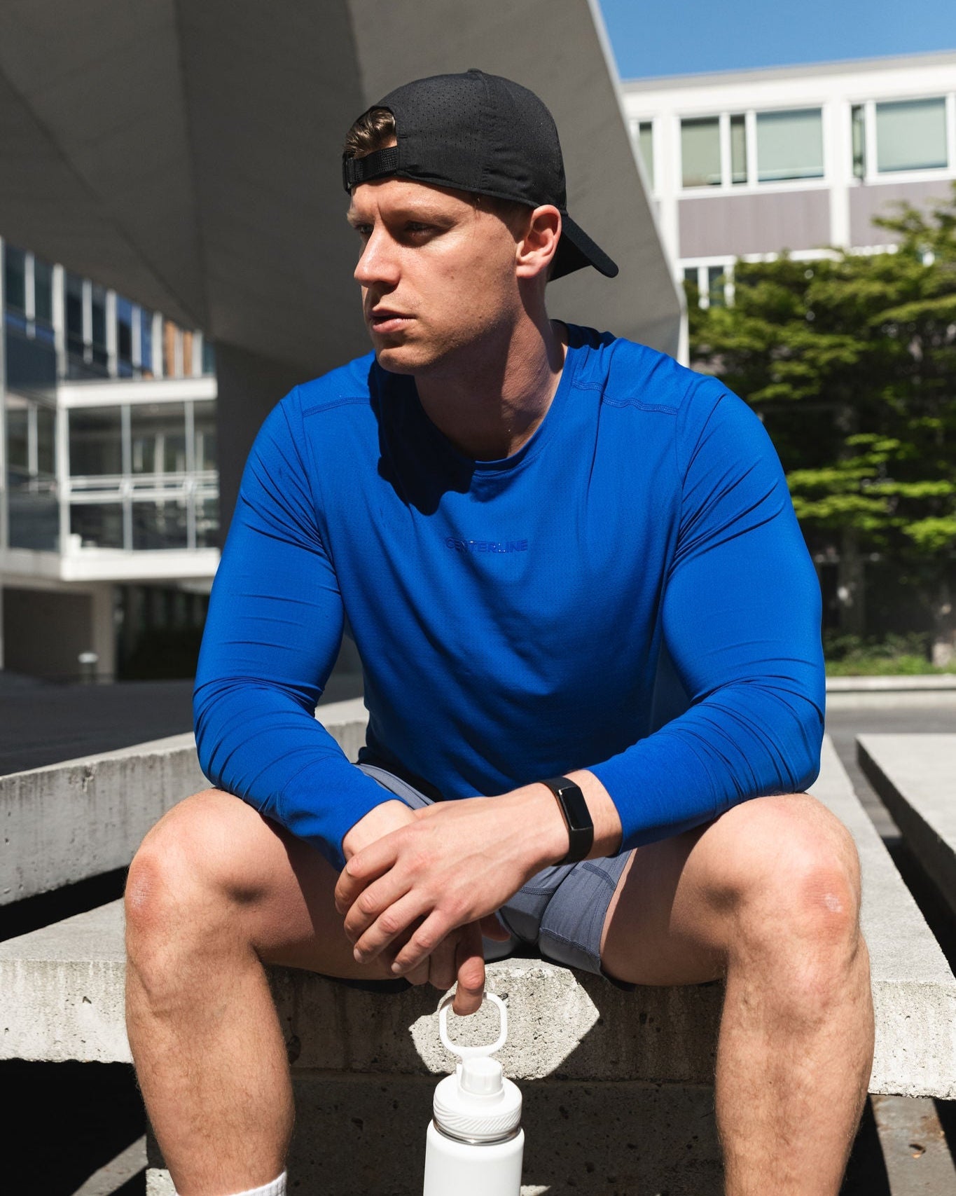 Man in blue shirt and hat sitting with water bottle.