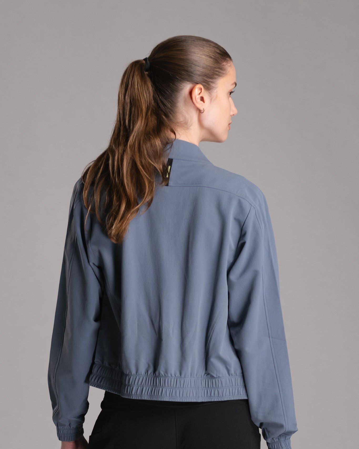 Woman from the back, wearing a gray-blue athletic jacket.