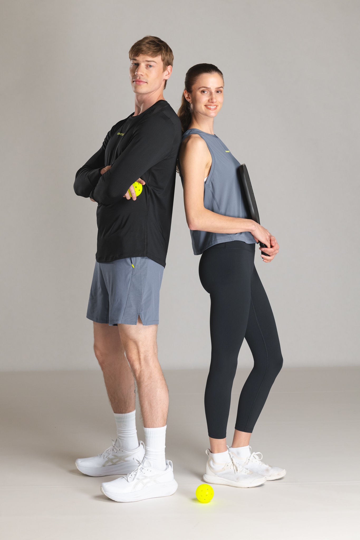 Two people in athletic wear standing back to back, one holding a pickleball.