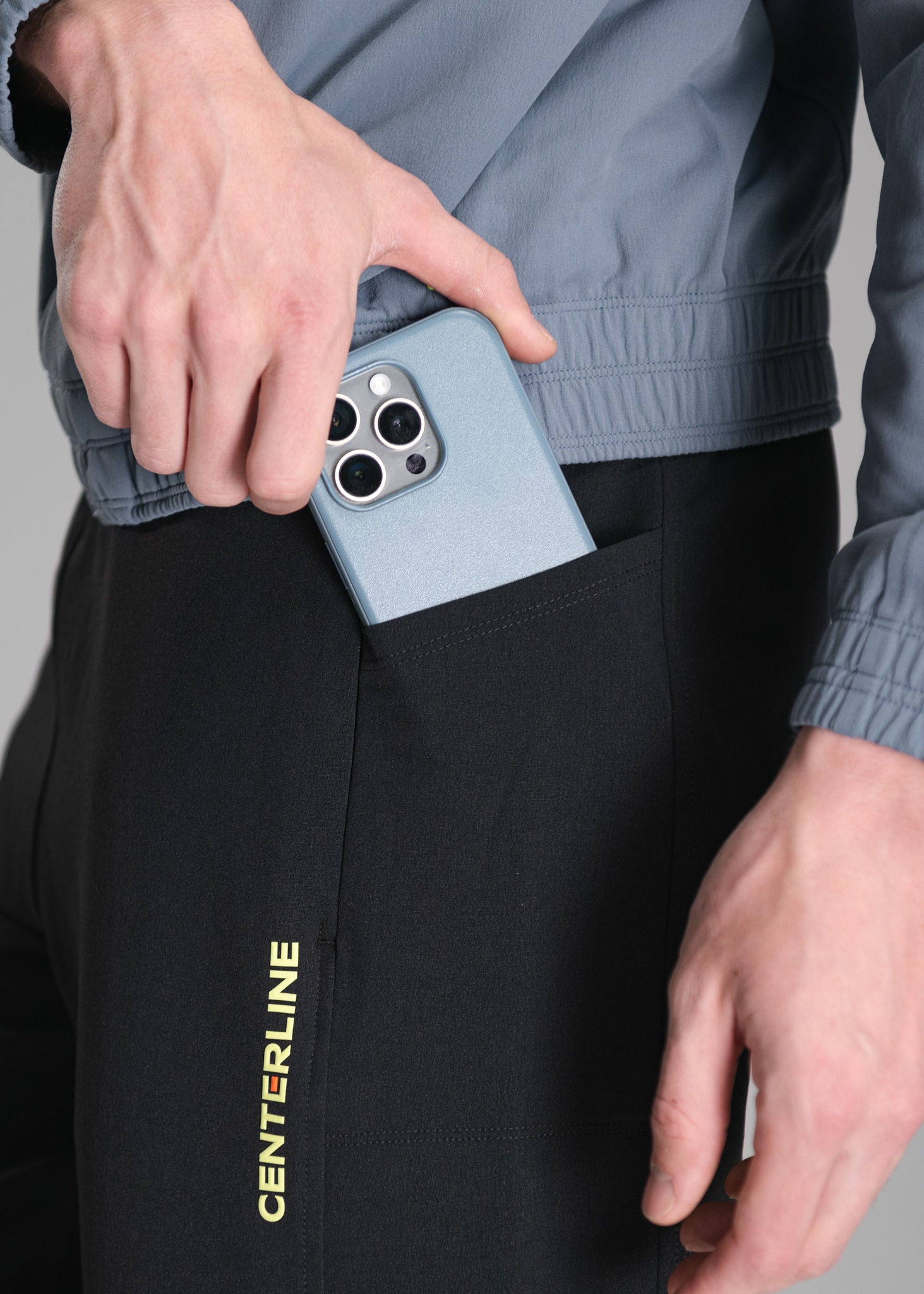 A person putting a blue phone in the pocket of black sweatpants, with a gray shirt.