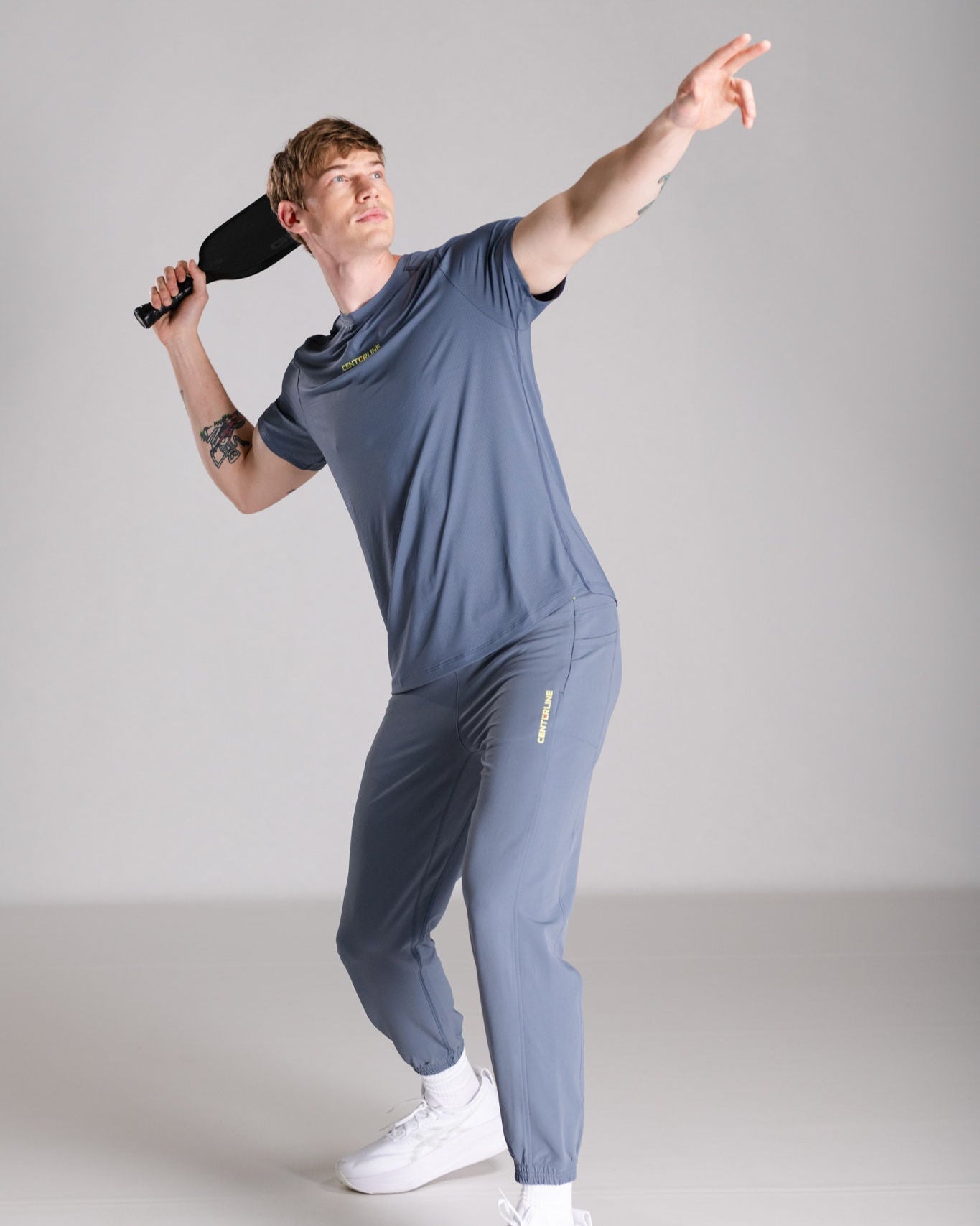 A man in a blue athletic outfit with a paddle in a studio setting.