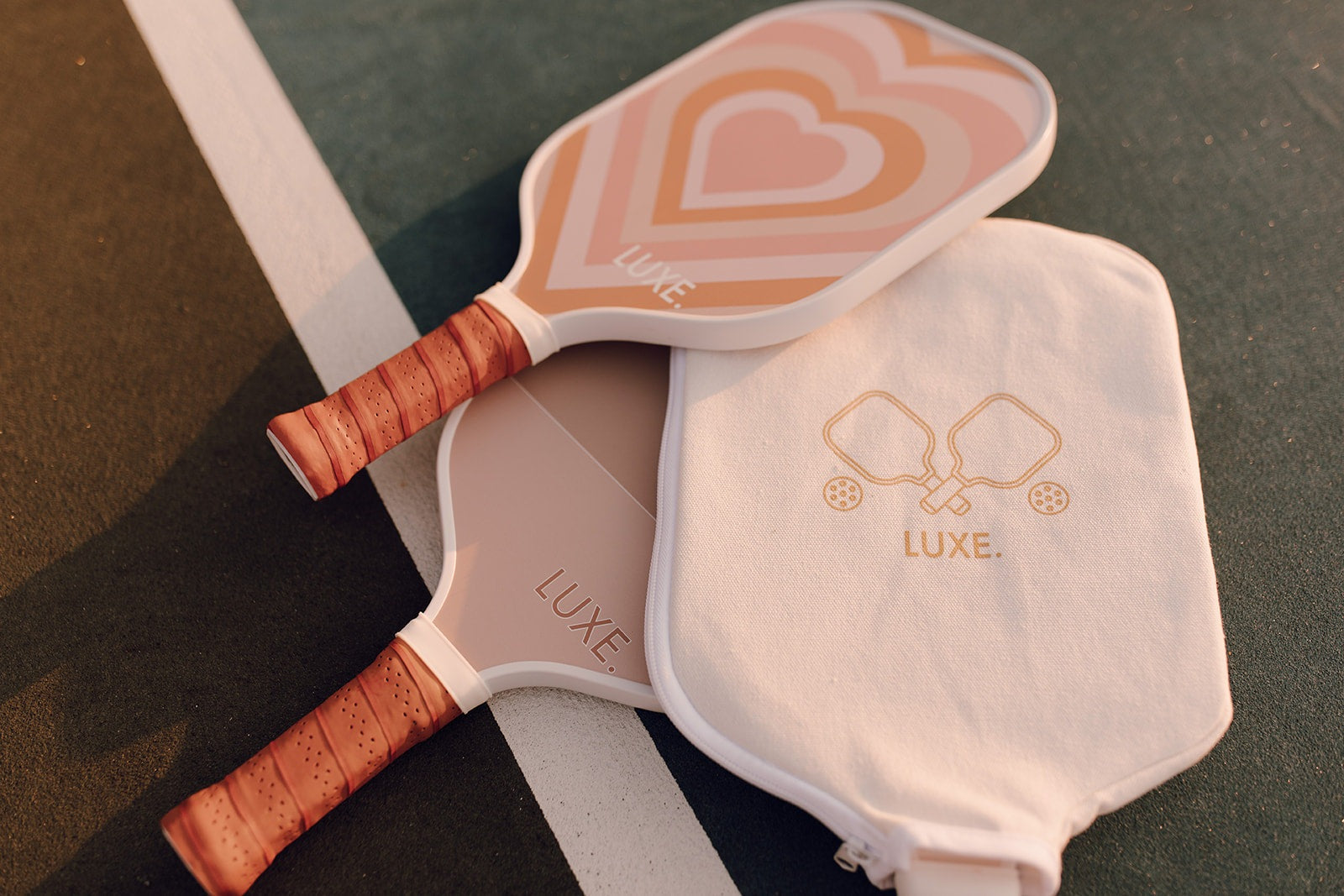 Two pickleball paddles with a heart design on one and a solid color on the other, a paddle cover, and a court.