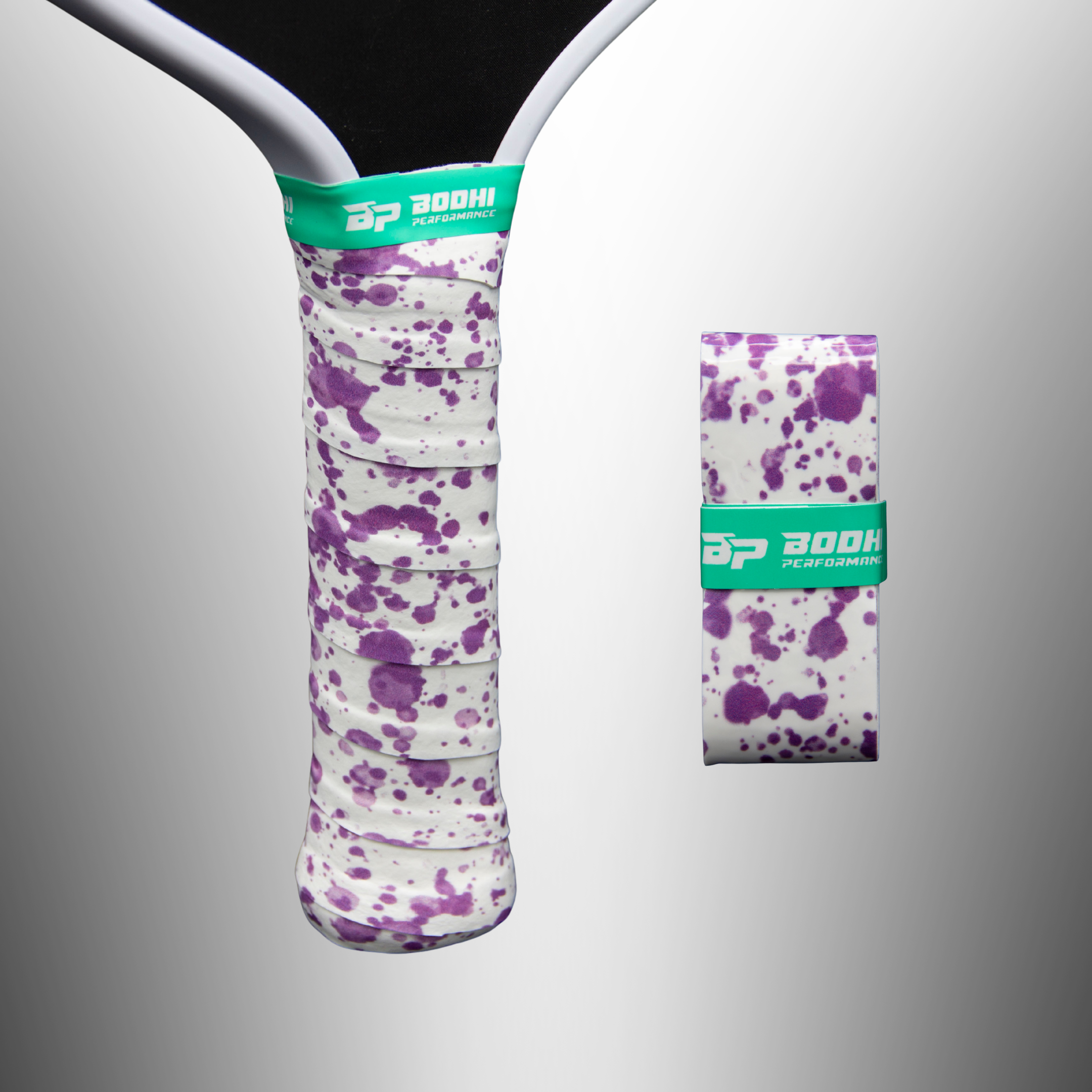 White paddle overgrip with purple splatter pattern by Bodhi Performance, wrapped on a handle, and a new rolled overgrip, both secured with green logo bands.