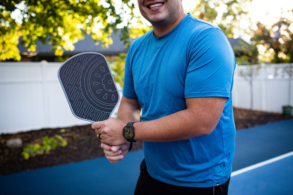 Man in blue t-shirt holding a pickleball paddle outdoors.