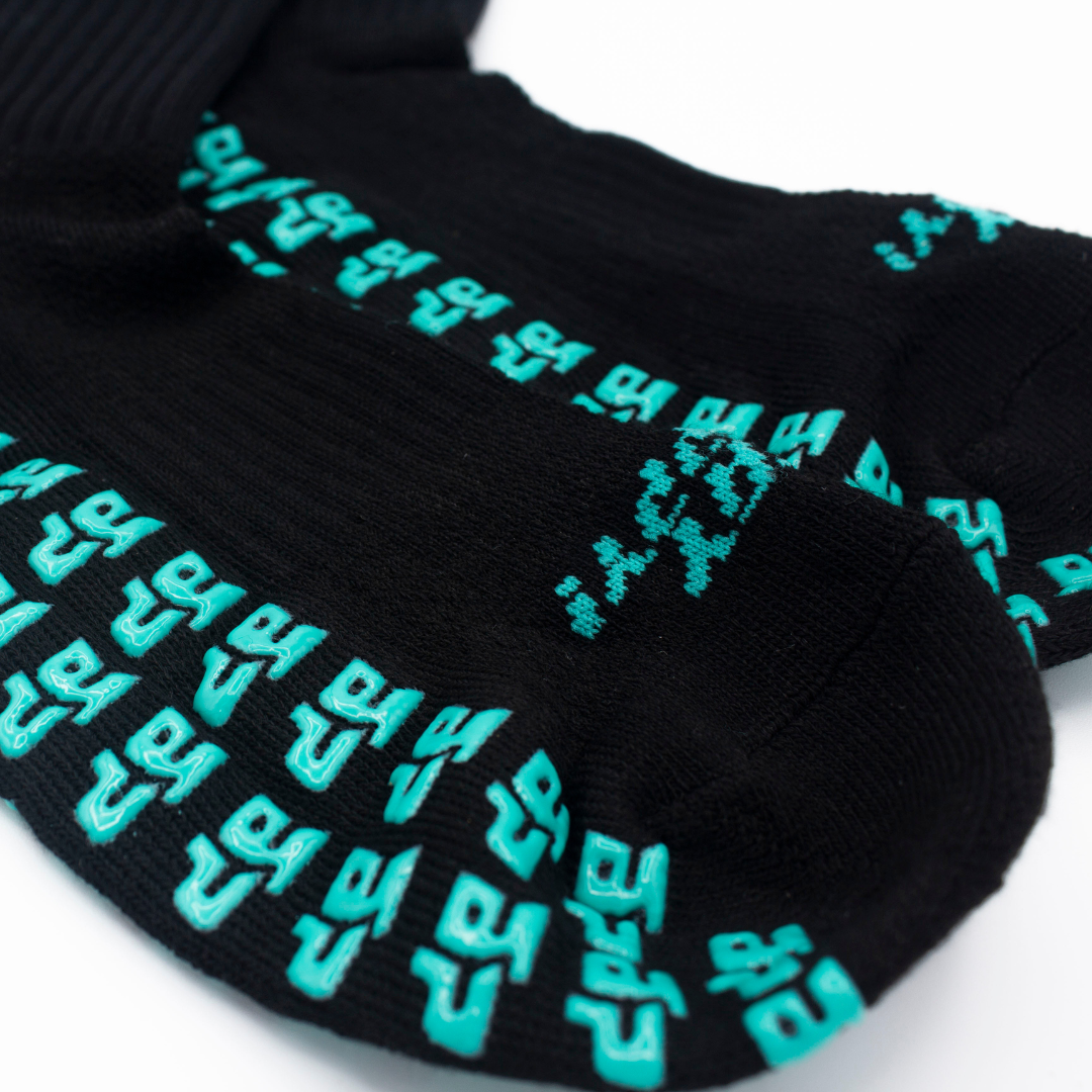 Black Unisex Performance Socks by Bodhi Performance with raised teal pixelated grip patterns on the sole.