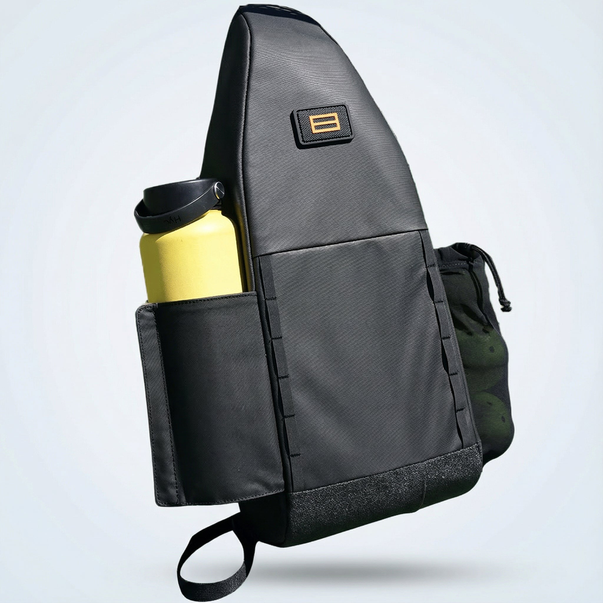 Black Cross Court Pickleball Sling by FORWRD, with a yellow water bottle, green pickleballs, a gold double bar logo, and a textured bottom.