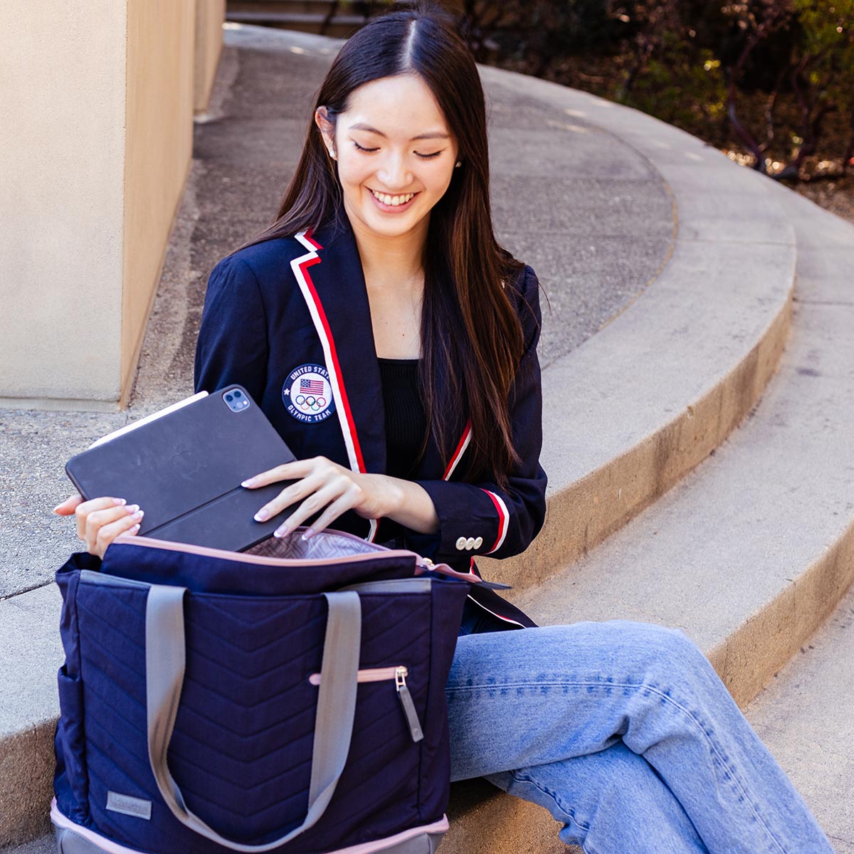 Navy quilted Pickleball Tote by Doubletake with grey handles and pink accents, held by a smiling woman placing a tablet inside.