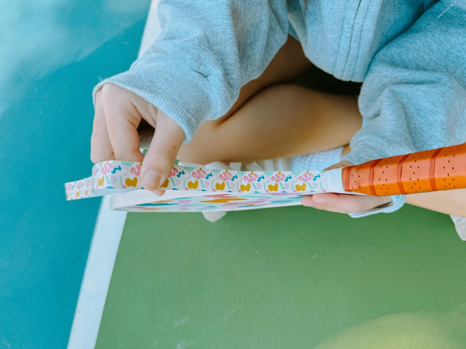 Person holding a pickleball paddle while seated on a court.