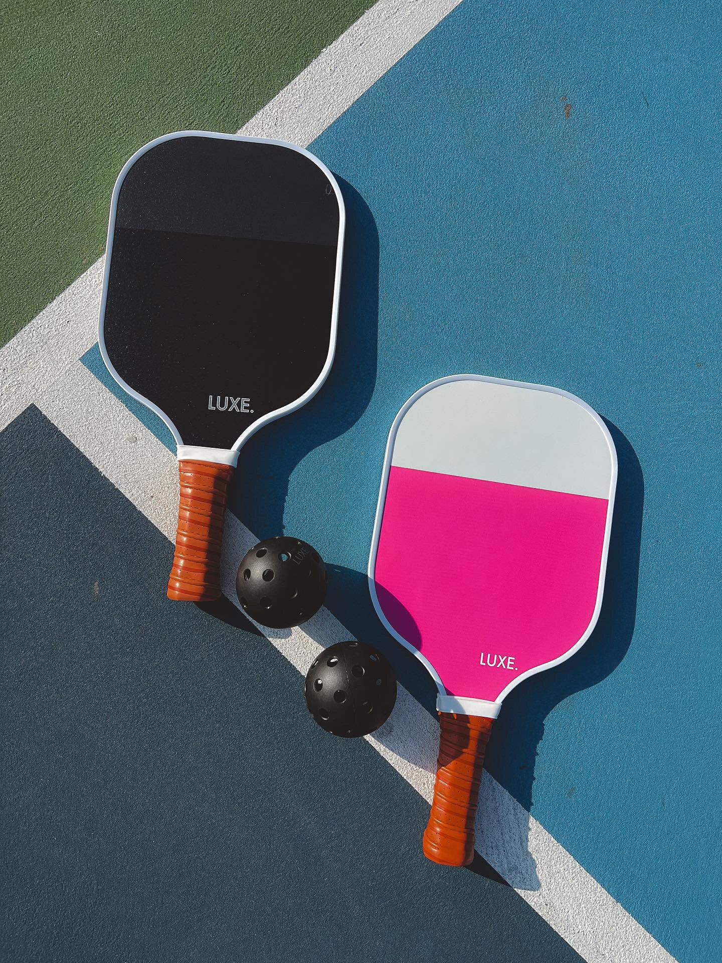 Two pickleball paddles and two balls on a blue, green, and white court.