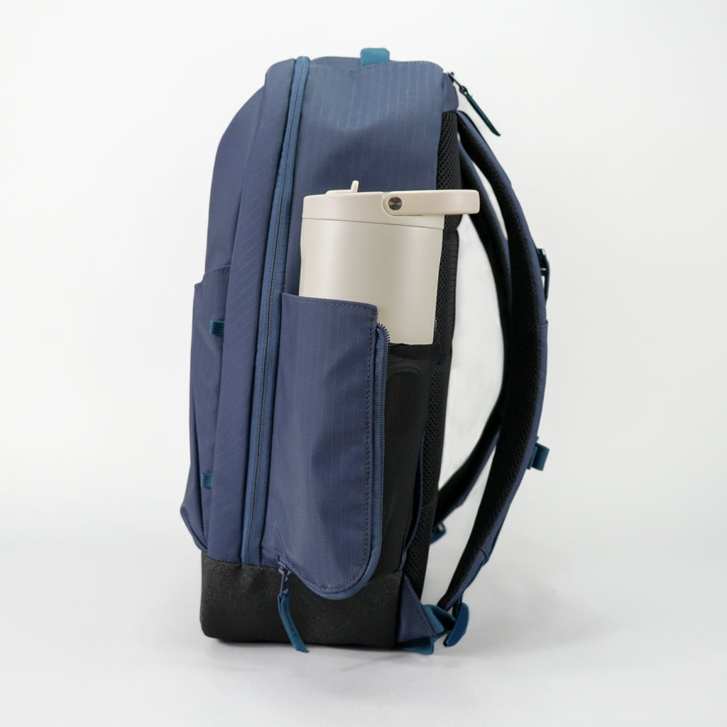 A blue backpack with a beige water bottle in its side pocket.