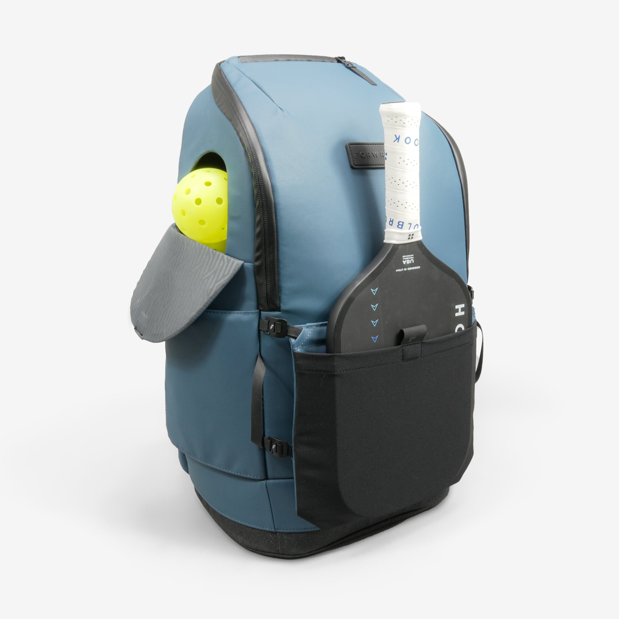 Blue pickleball backpack by FORWRD, holding a yellow pickleball and gray slipper in an open pocket, with a black paddle in a side pocket.