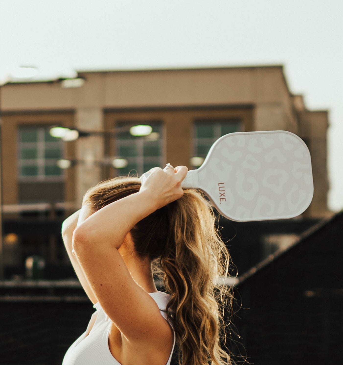 Woman tying her hair with a white hairbrush against a building background.