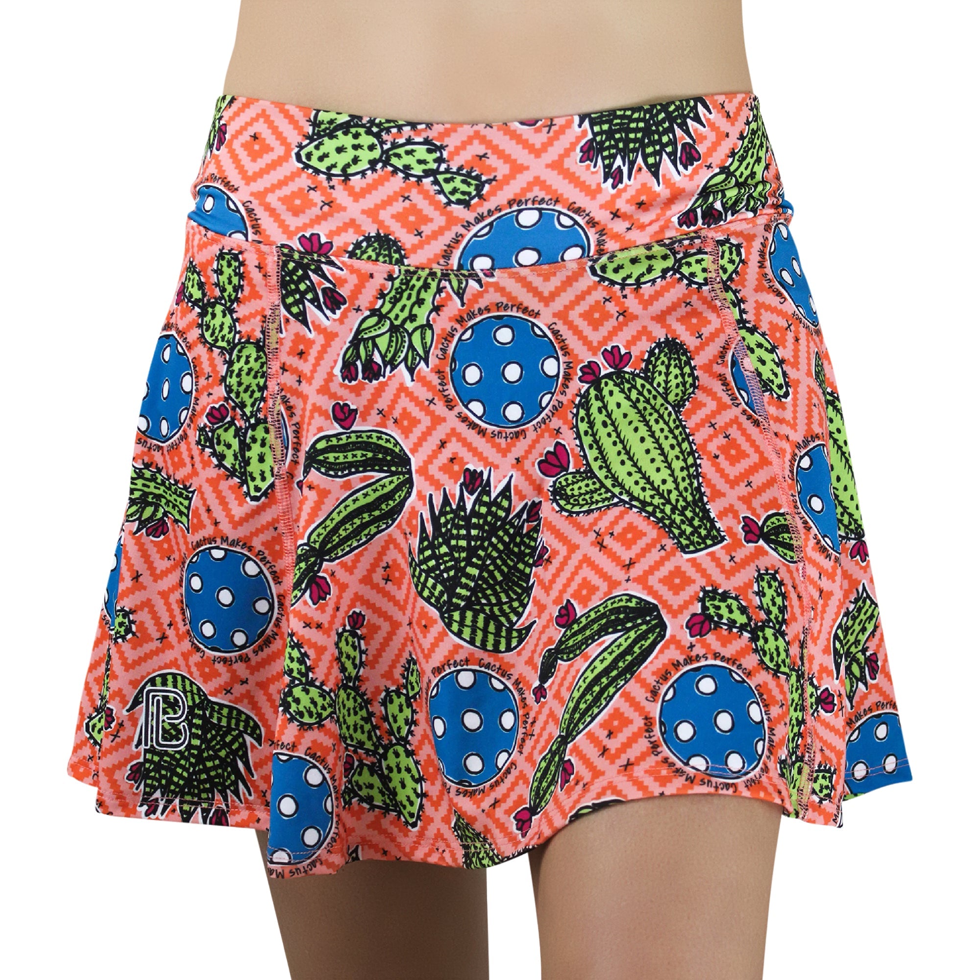 Orange-pink A-line skort by Pickleball Bella, featuring cactus, succulent, and blue polka dot patterns, with 'Cactus Makes Perfect' text and a geometric background.