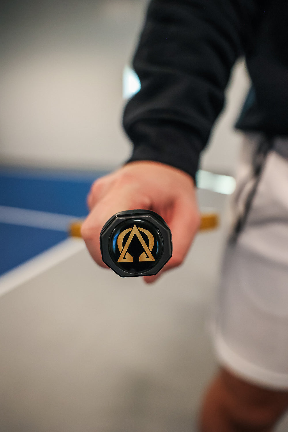 Person holding a black and gold tennis racket. The person wears a black jacket and white shorts.