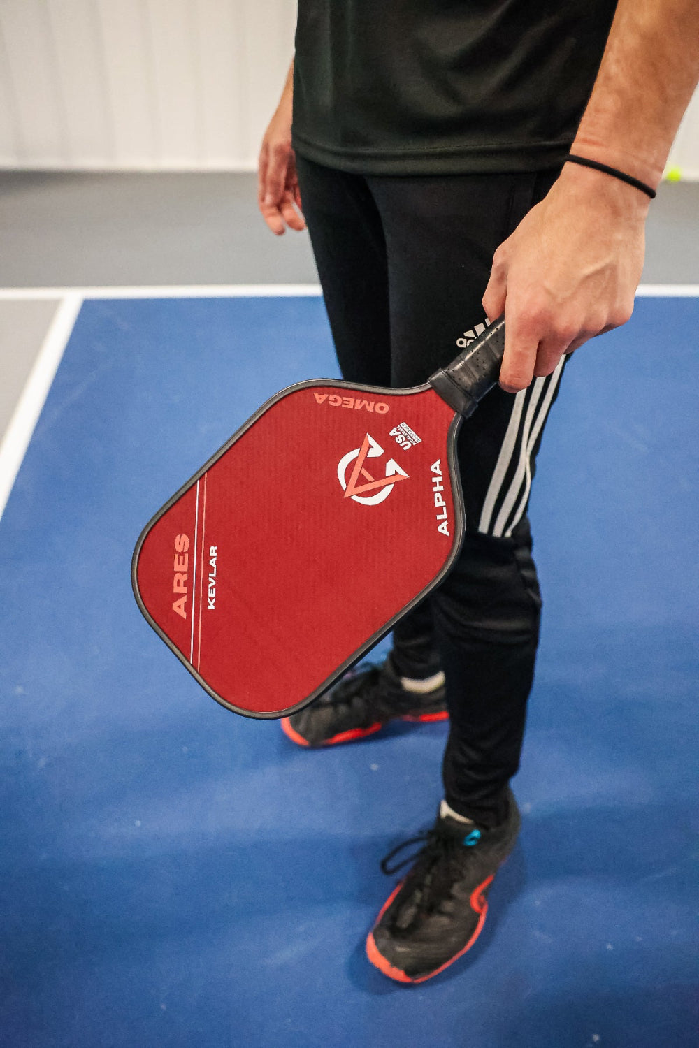 A person in black athletic wear holding a red pickleball paddle.