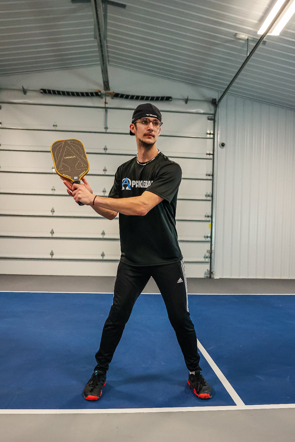 Man in black athletic wear holding a pickleball paddle indoors.