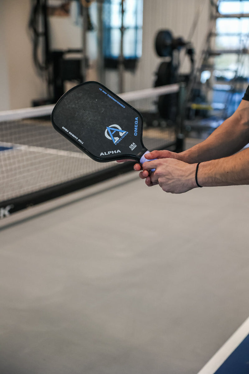 A person holding a black pickleball paddle with blue accents.