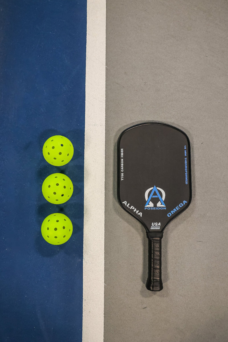 Three yellow pickleballs and a black paddle on a court.