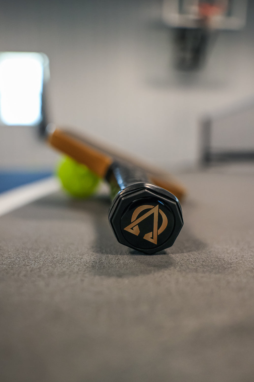 Close-up of a black and gold paddle ball racket resting on a gray surface with a green ball.