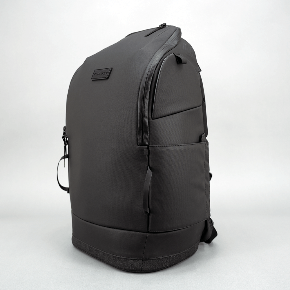 Dark grey pickleball backpack by FORWRD with a zippered main compartment, side pocket, and textured bottom, shown from the side.