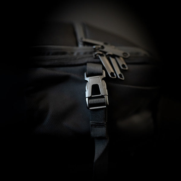 Black textured backpack by EngagePickleball, showing a black plastic buckle, strap, and metal zipper pulls.