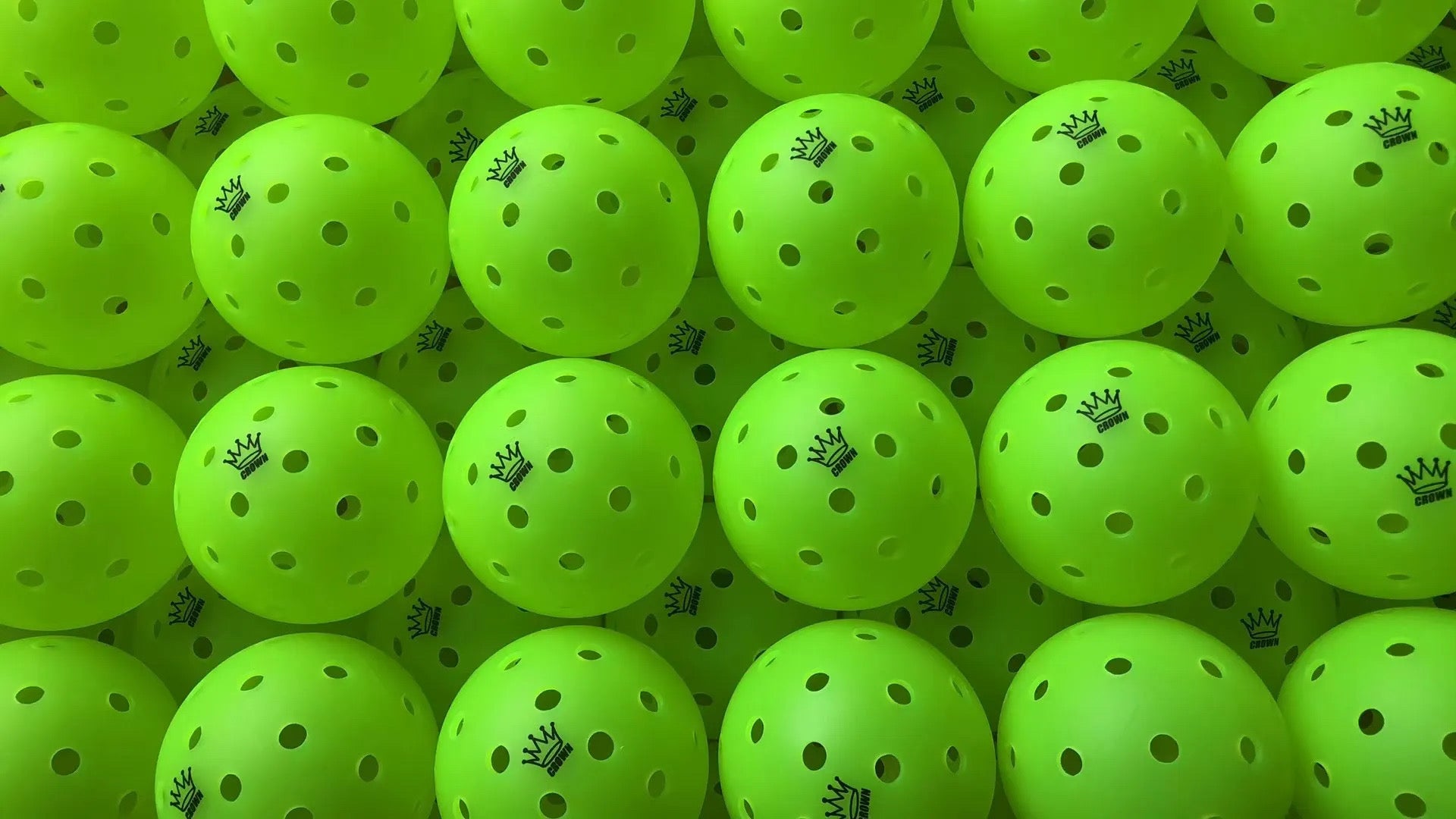 Pile of yellow-green pickleballs, each with a small crown logo and perforated holes.