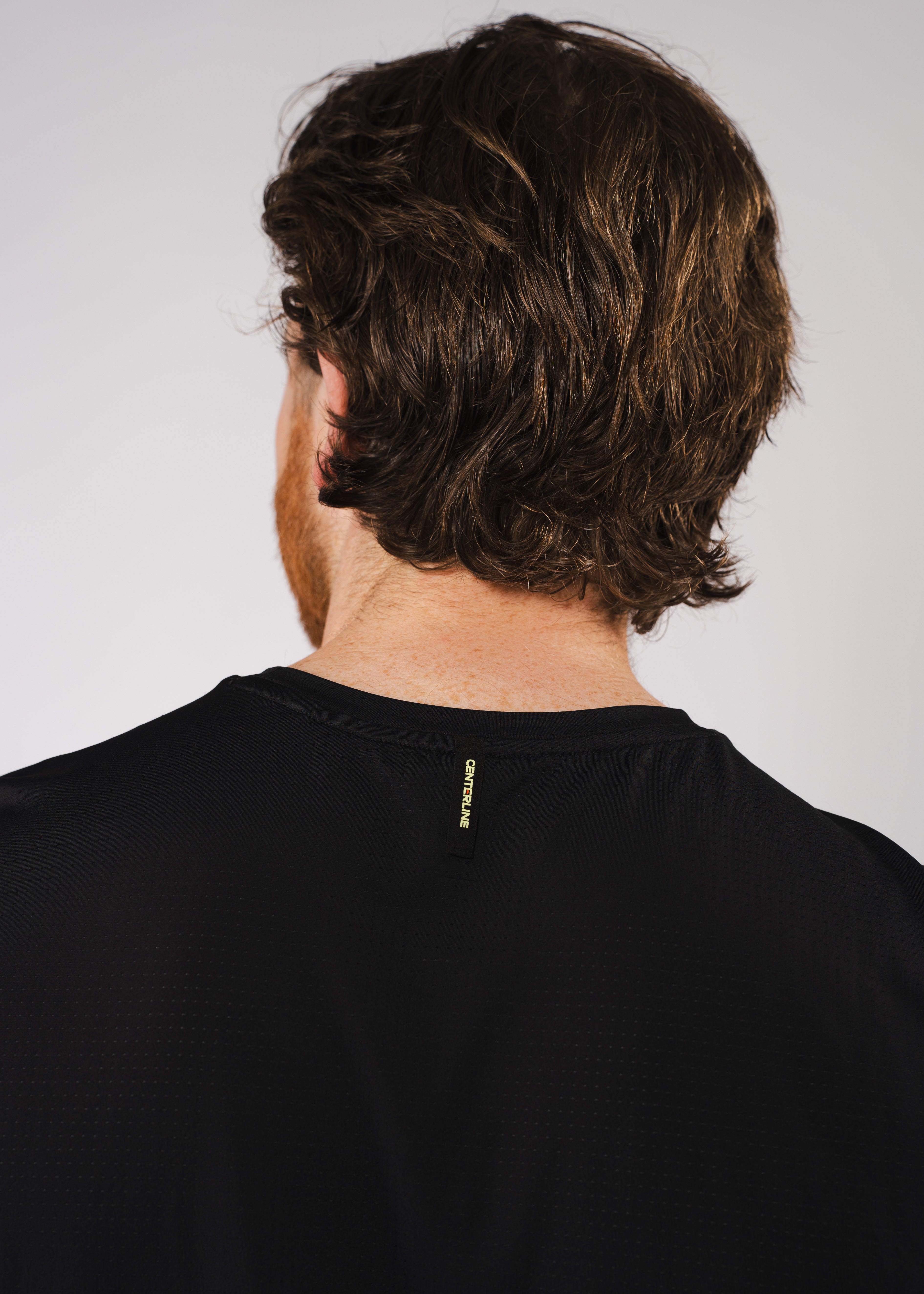 Back view of a man with brown hair wearing a black mesh shirt with "CENTERLINE" label.