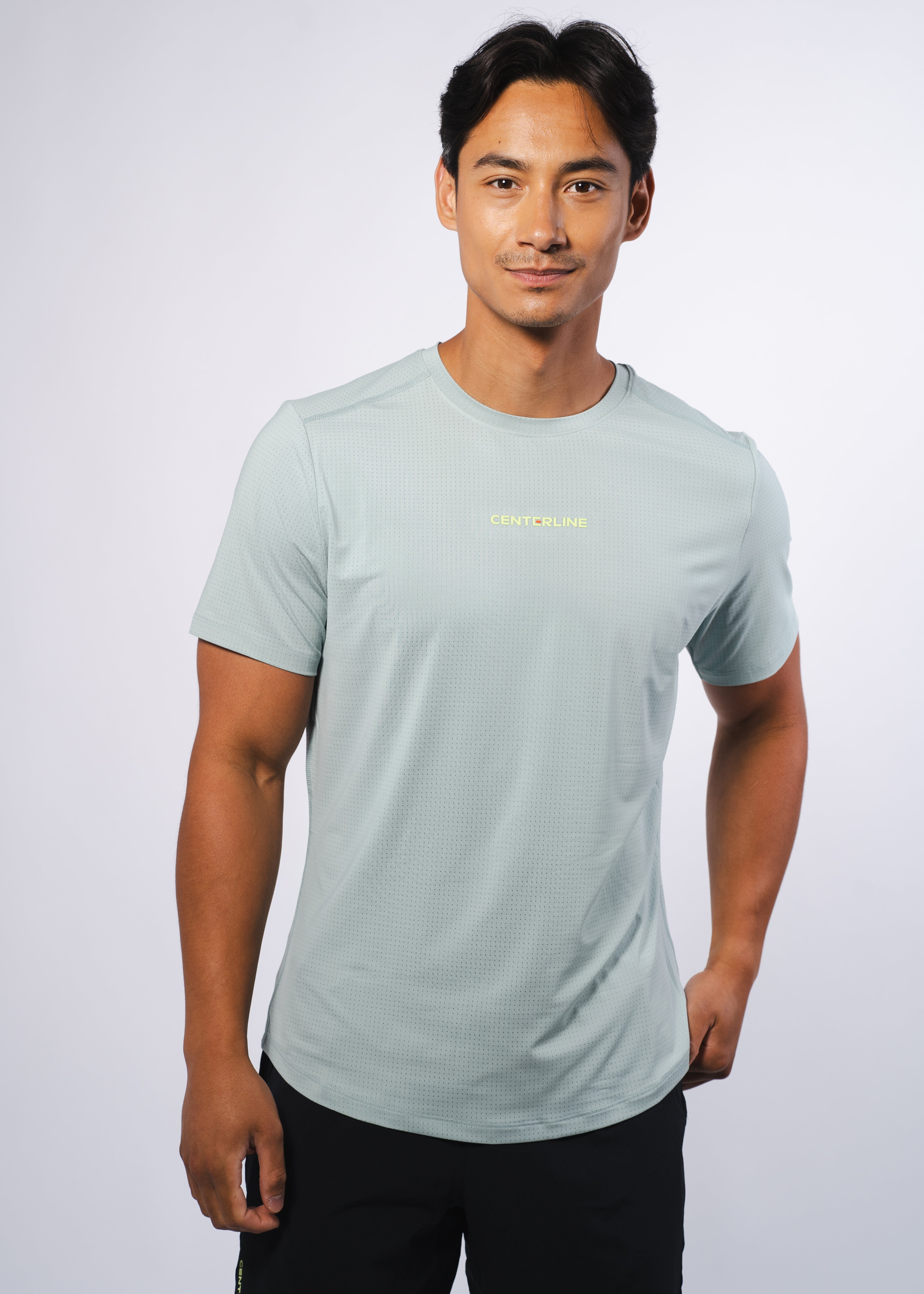 Perforated light mint green Men's AirLite Tee by Centerline Athletics, featuring a neon yellow "CENTERLINE" logo on the chest, worn by a man in black shorts.