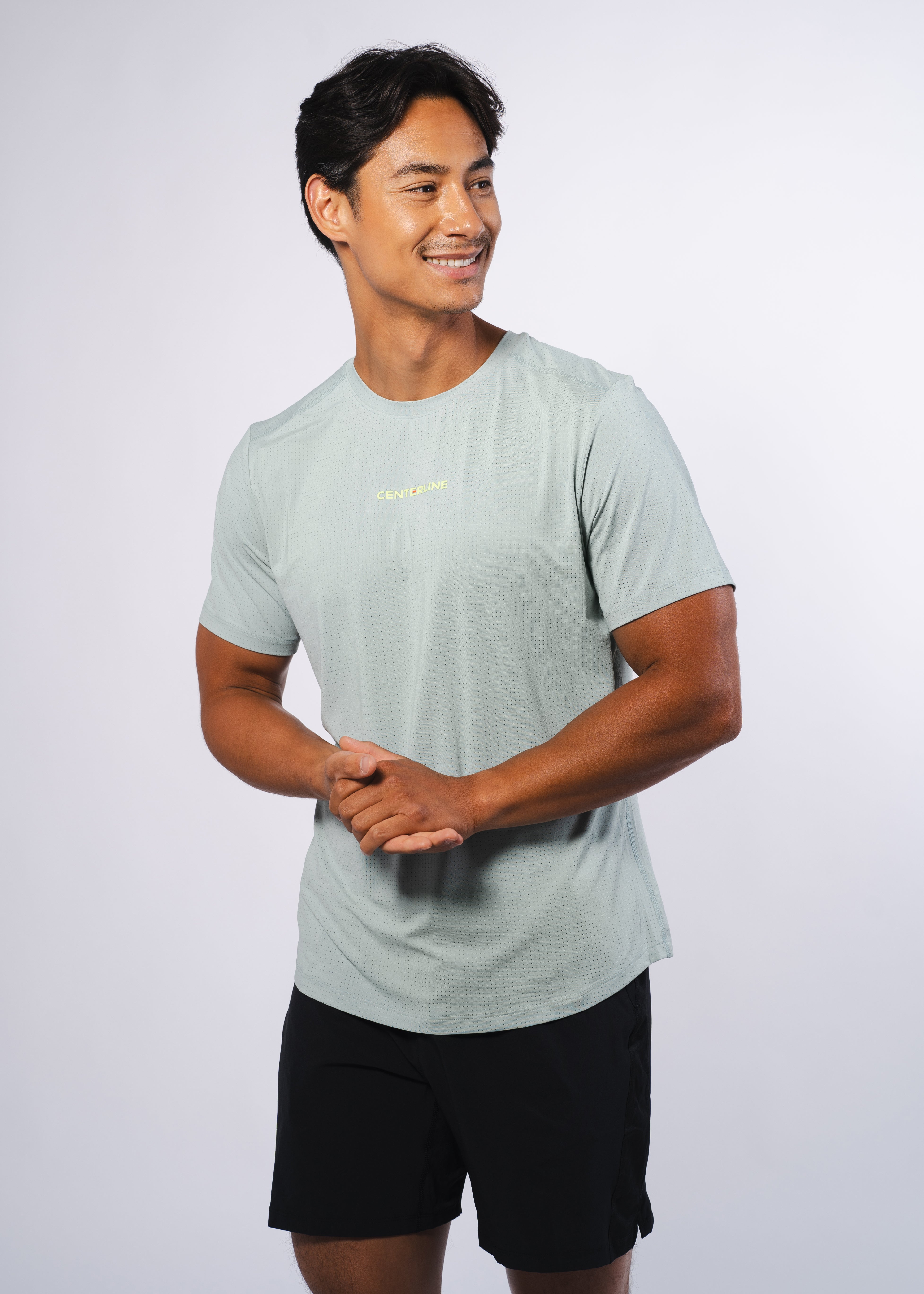 Man in pale green shirt and black shorts, hands clasped.