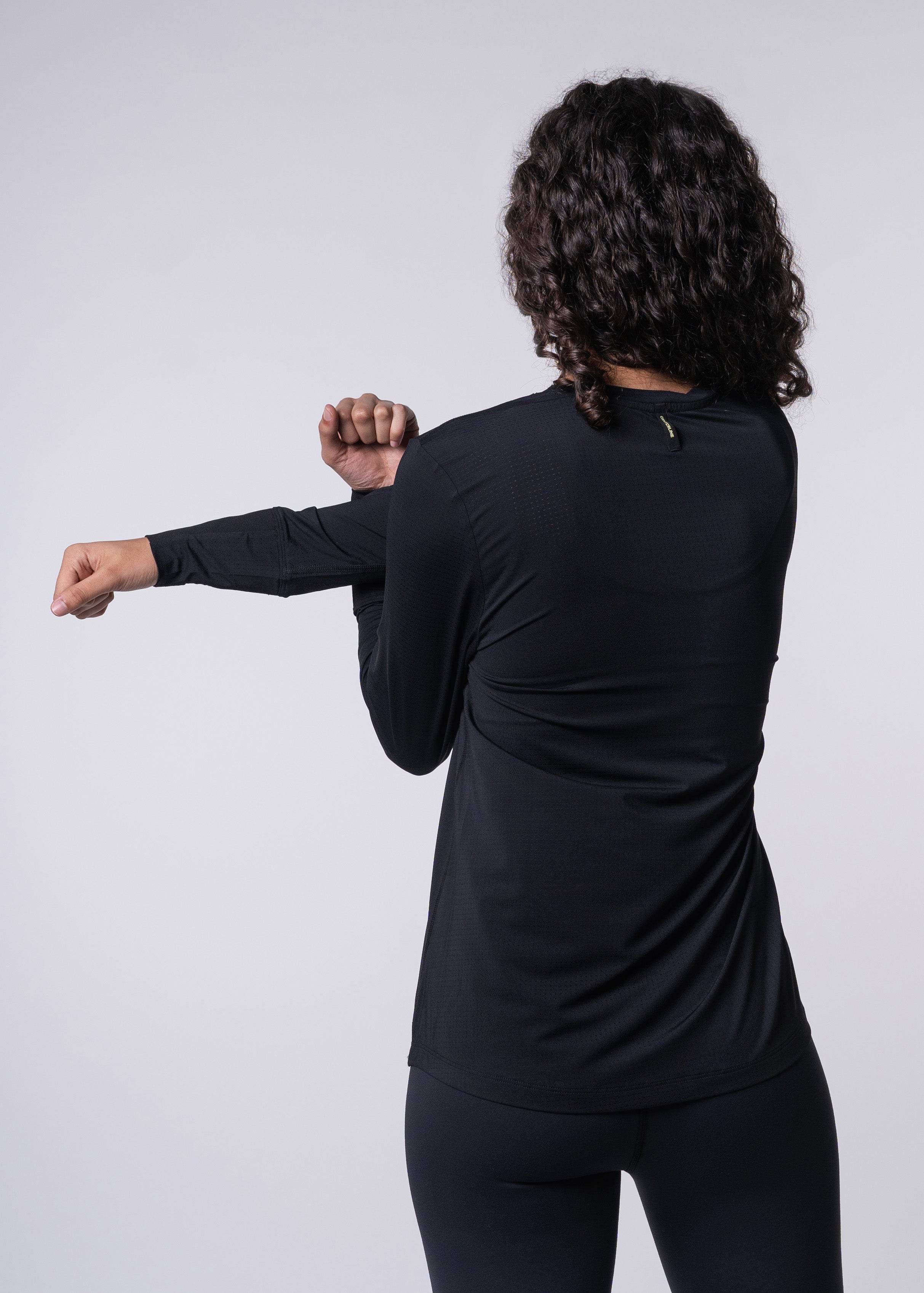 A woman in black athletic clothing stretches her arm across her chest.