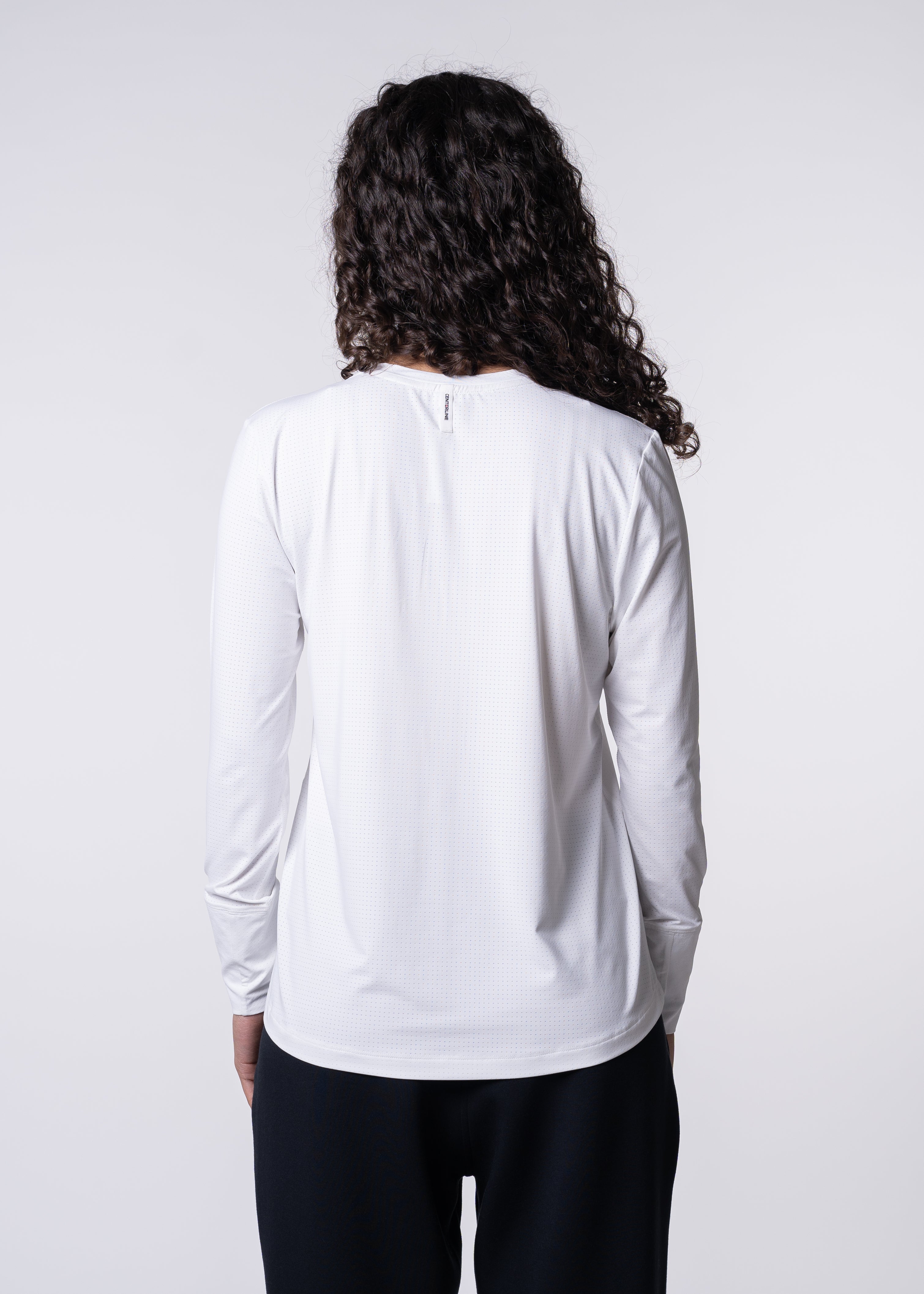 Back view of a woman wearing a white, long-sleeved shirt and dark pants.