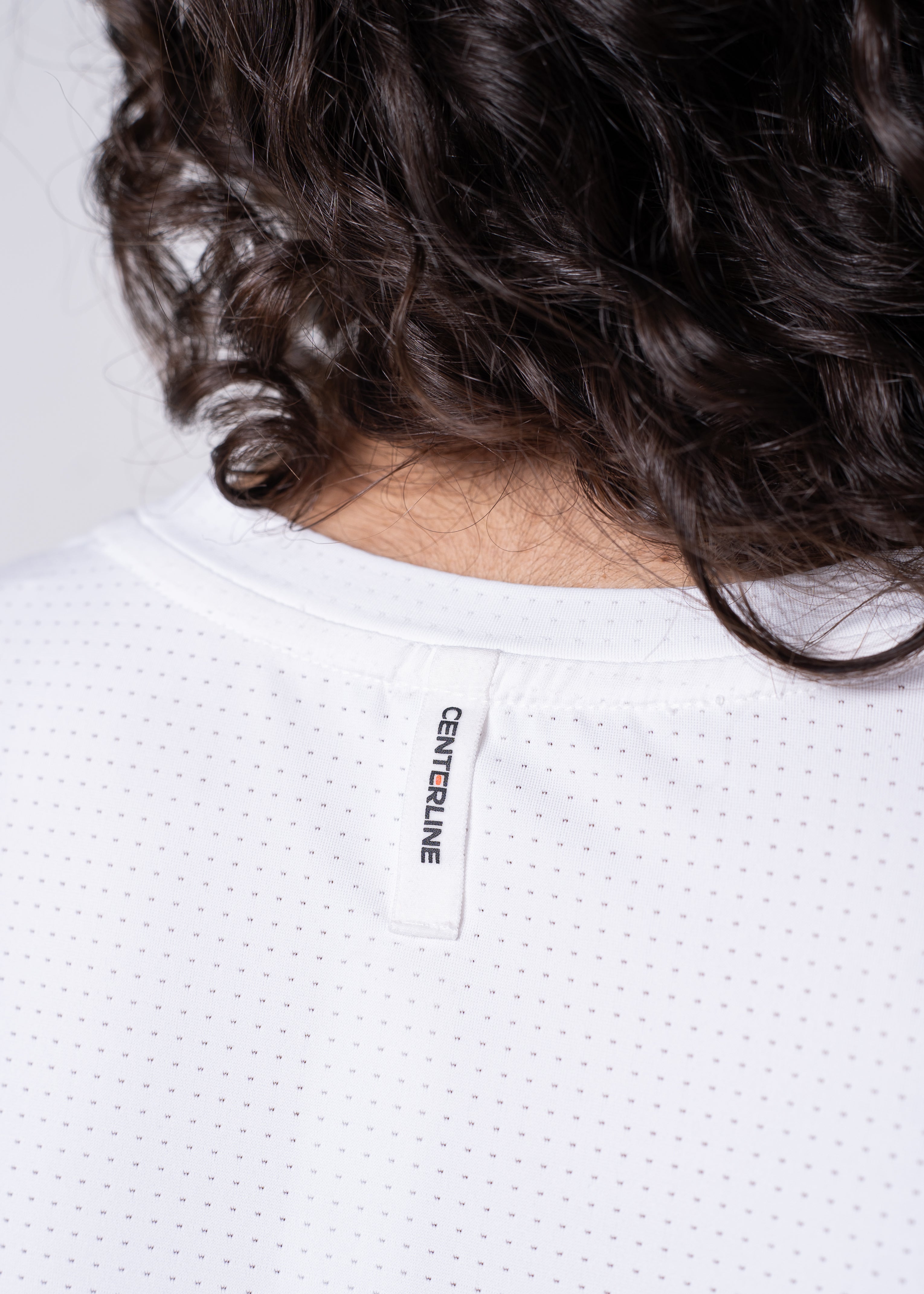 Close-up of a white, dotted, mesh shirt with a "CENTERLINE" tag on the collar. Dark brown, curly hair is visible above the shirt.
