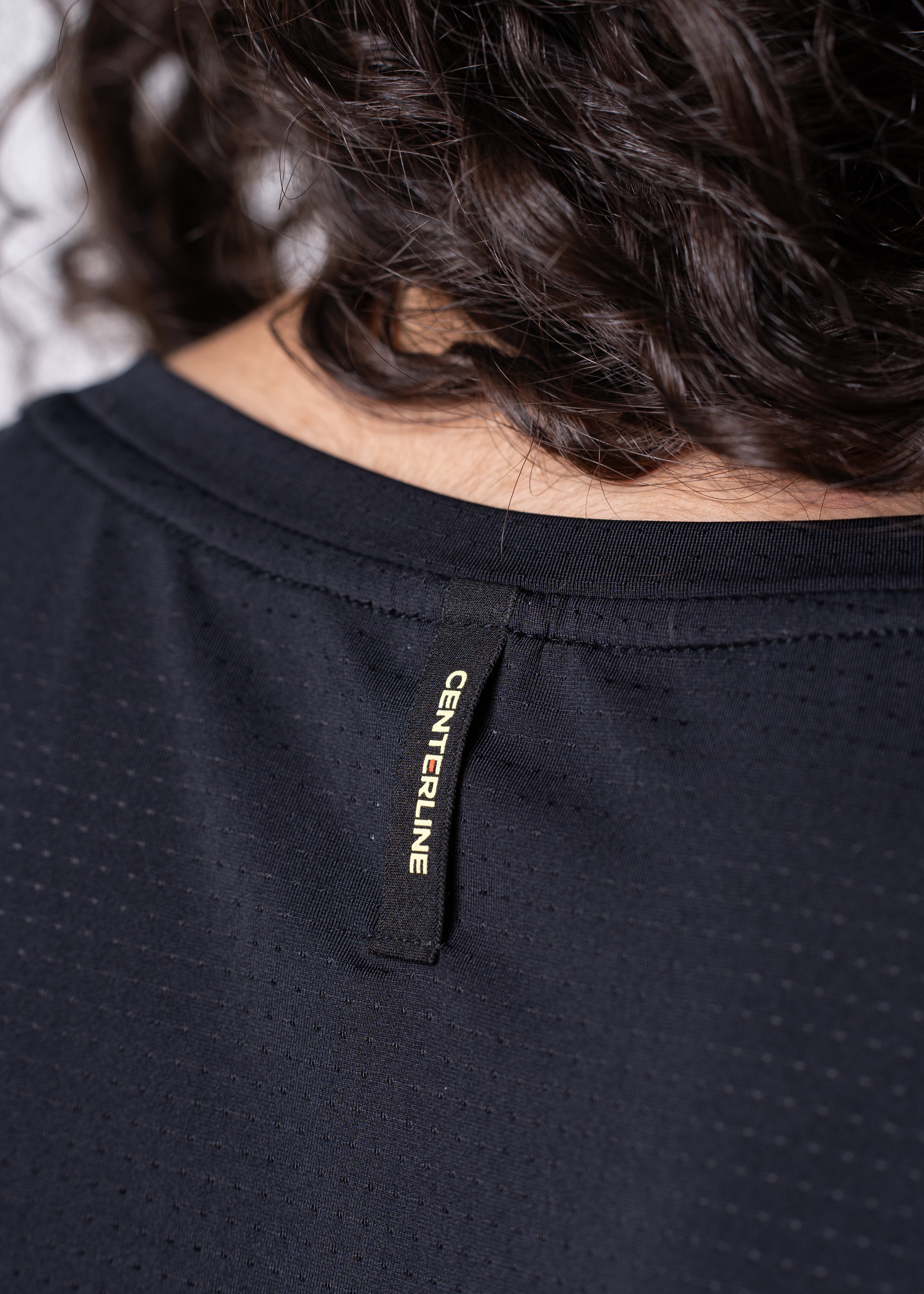 Close-up of a person's back in a black mesh shirt with "CENTERLINE" label.