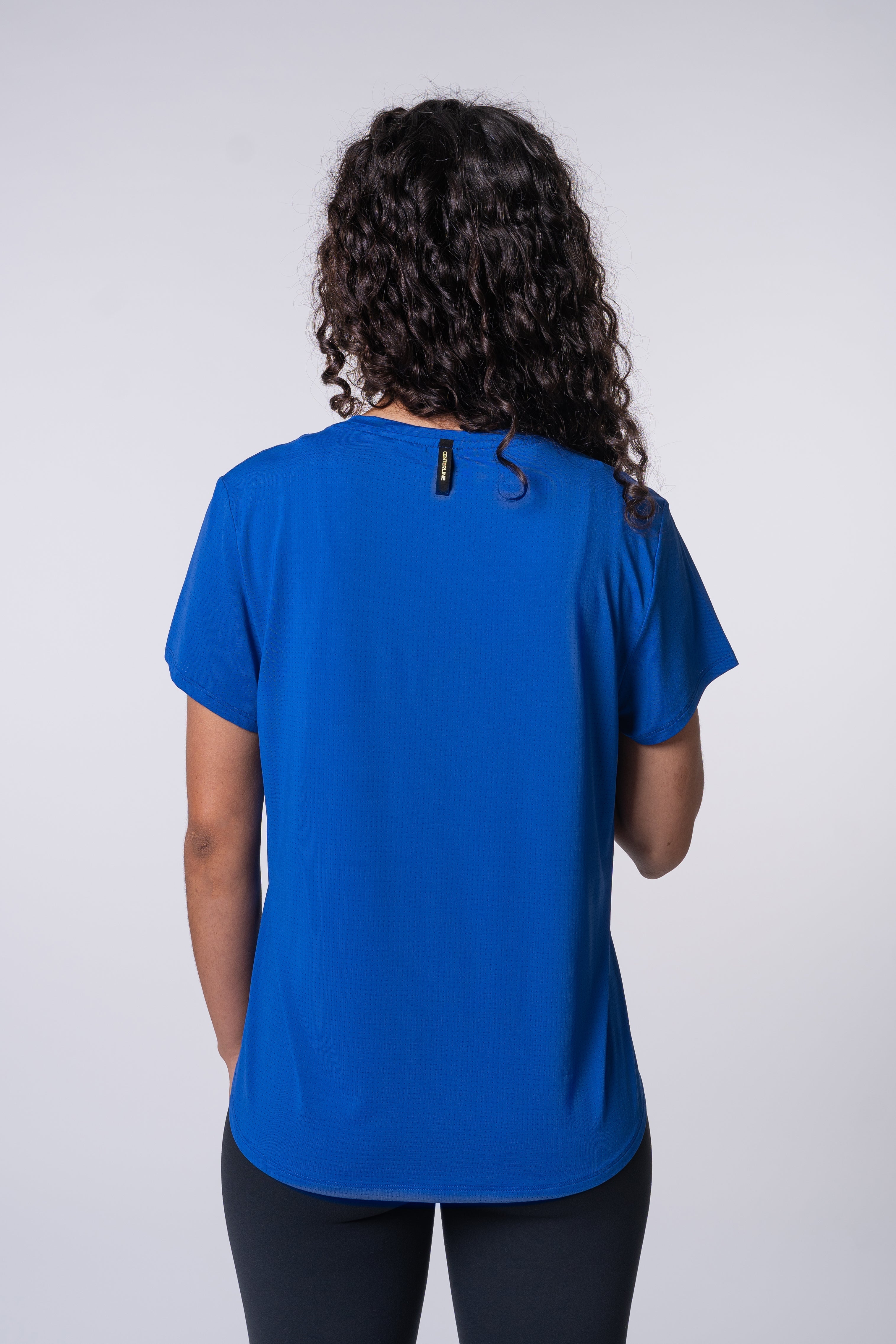 Back view of a woman wearing a blue t-shirt and black leggings, standing against a white background.