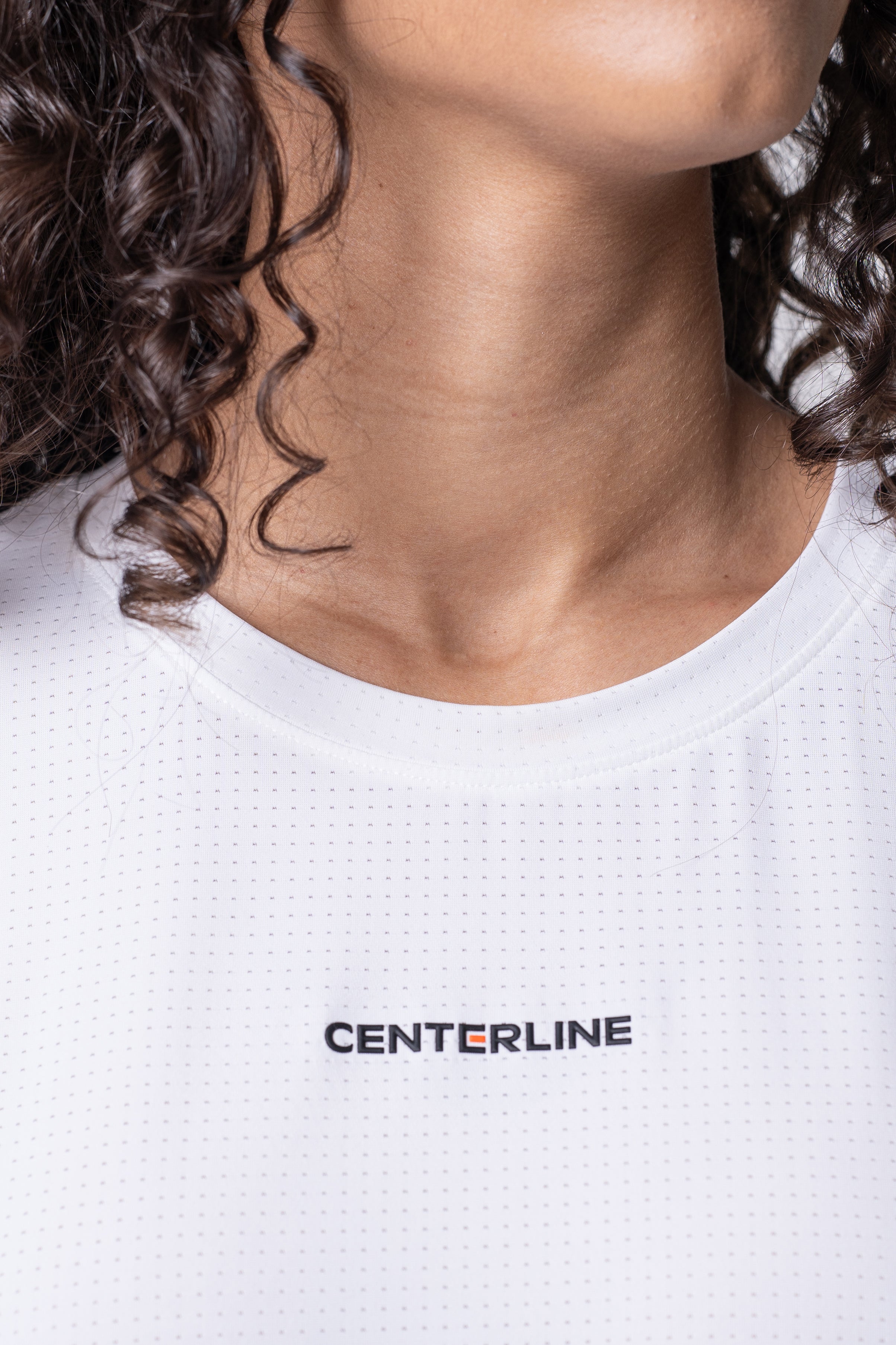 Close-up of a person wearing a white shirt with the word "CENTERLINE" printed on it. The shirt has a subtle grid pattern, and the person has curly dark hair.