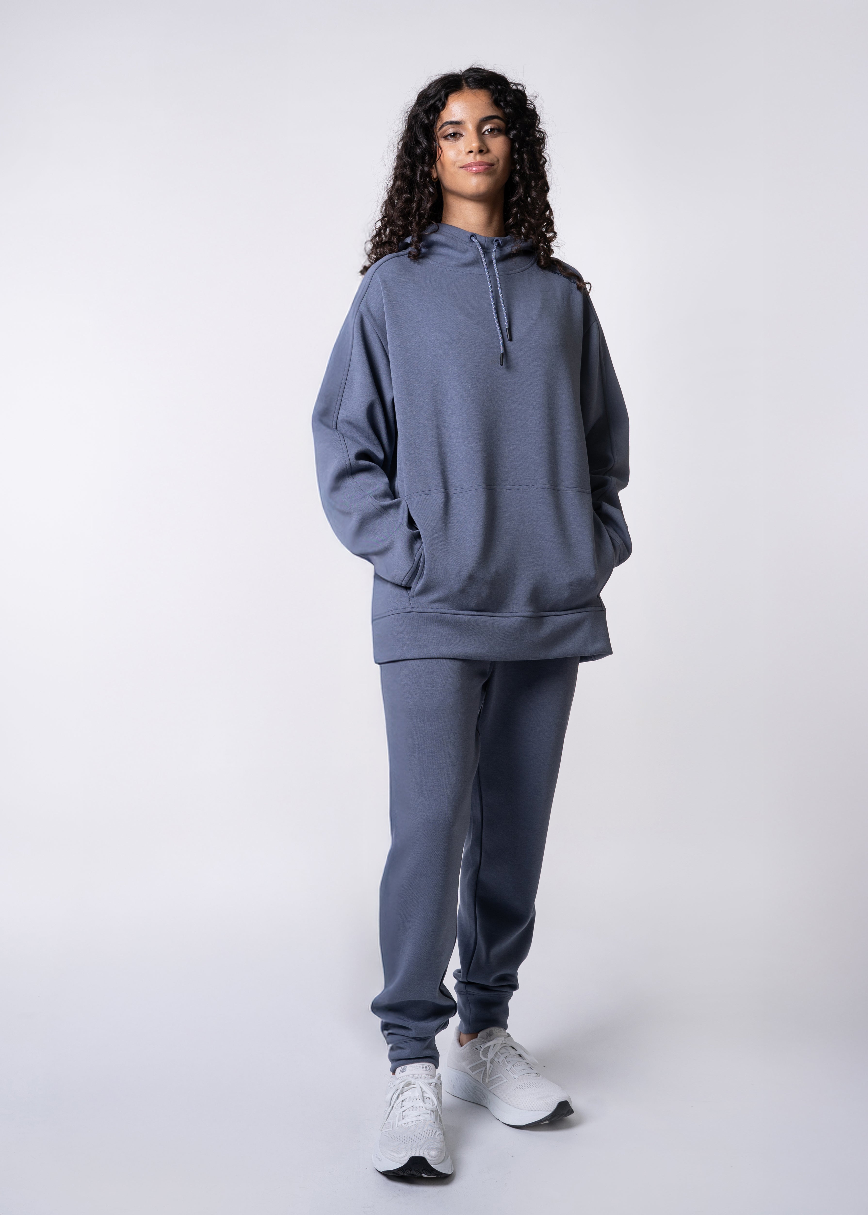 Woman in blue hoodie and sweatpants with white sneakers.