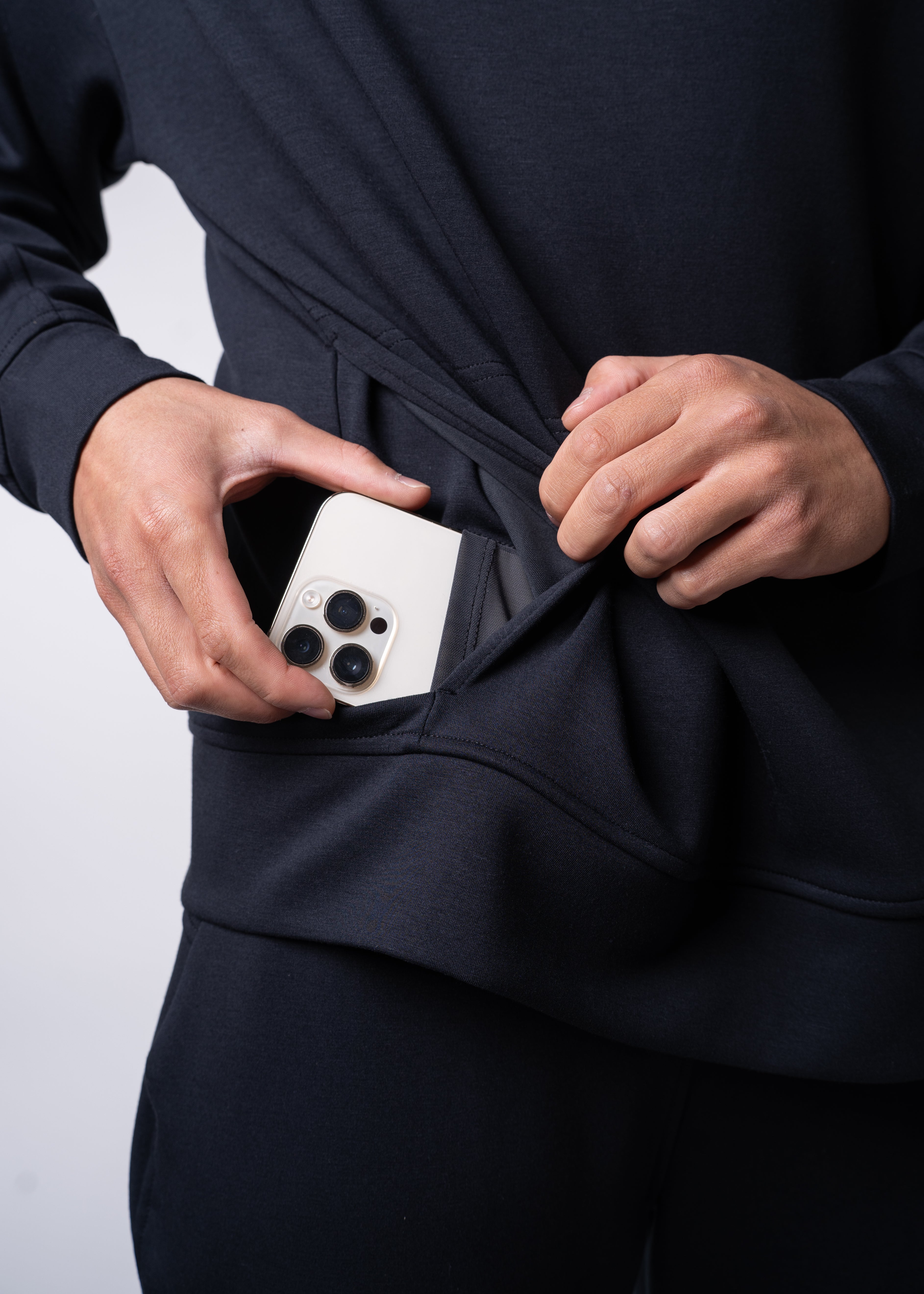 Person putting a smartphone in a black hoodie pocket.