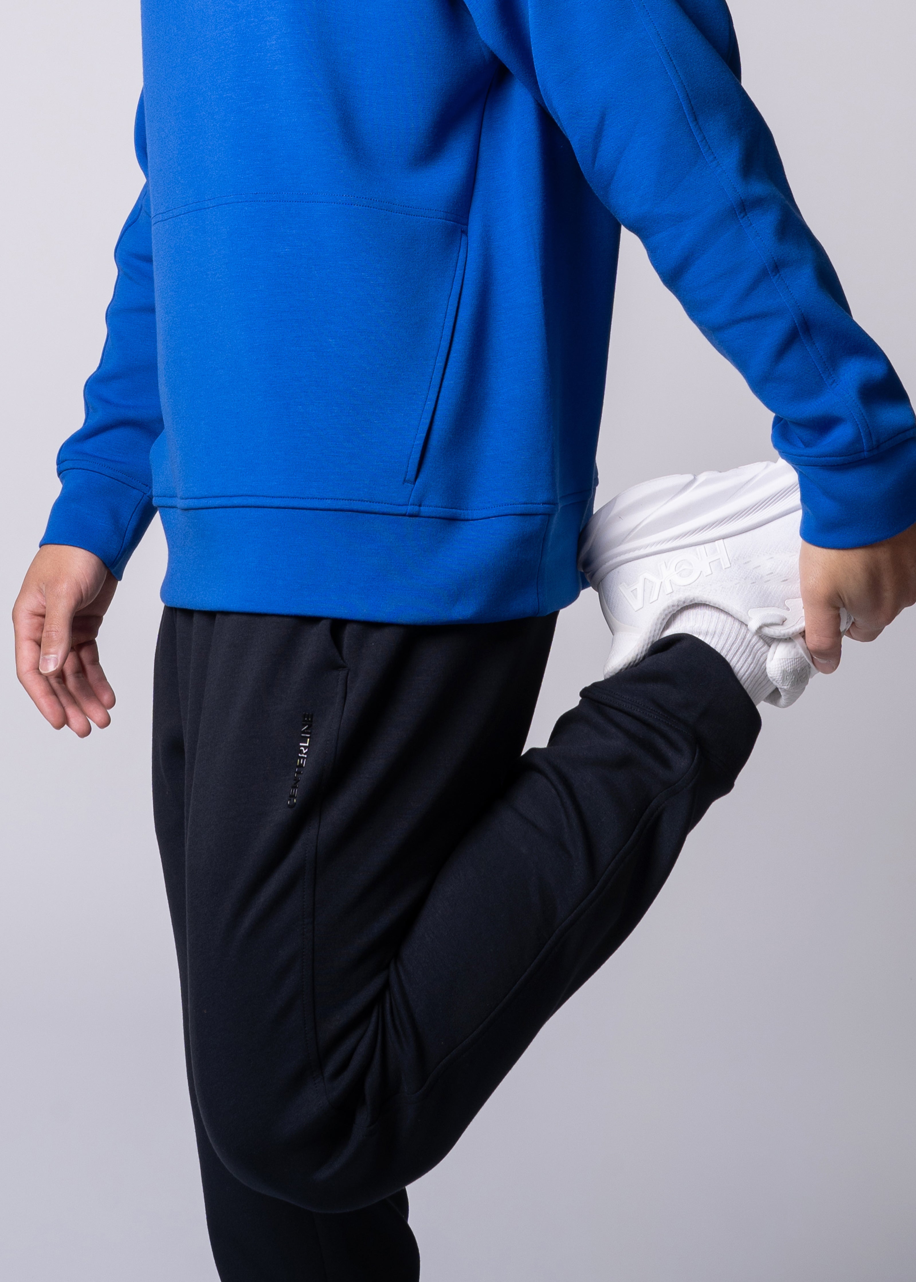 Person stretching wearing a blue hoodie, black sweatpants, white socks, and Hoka sneakers.