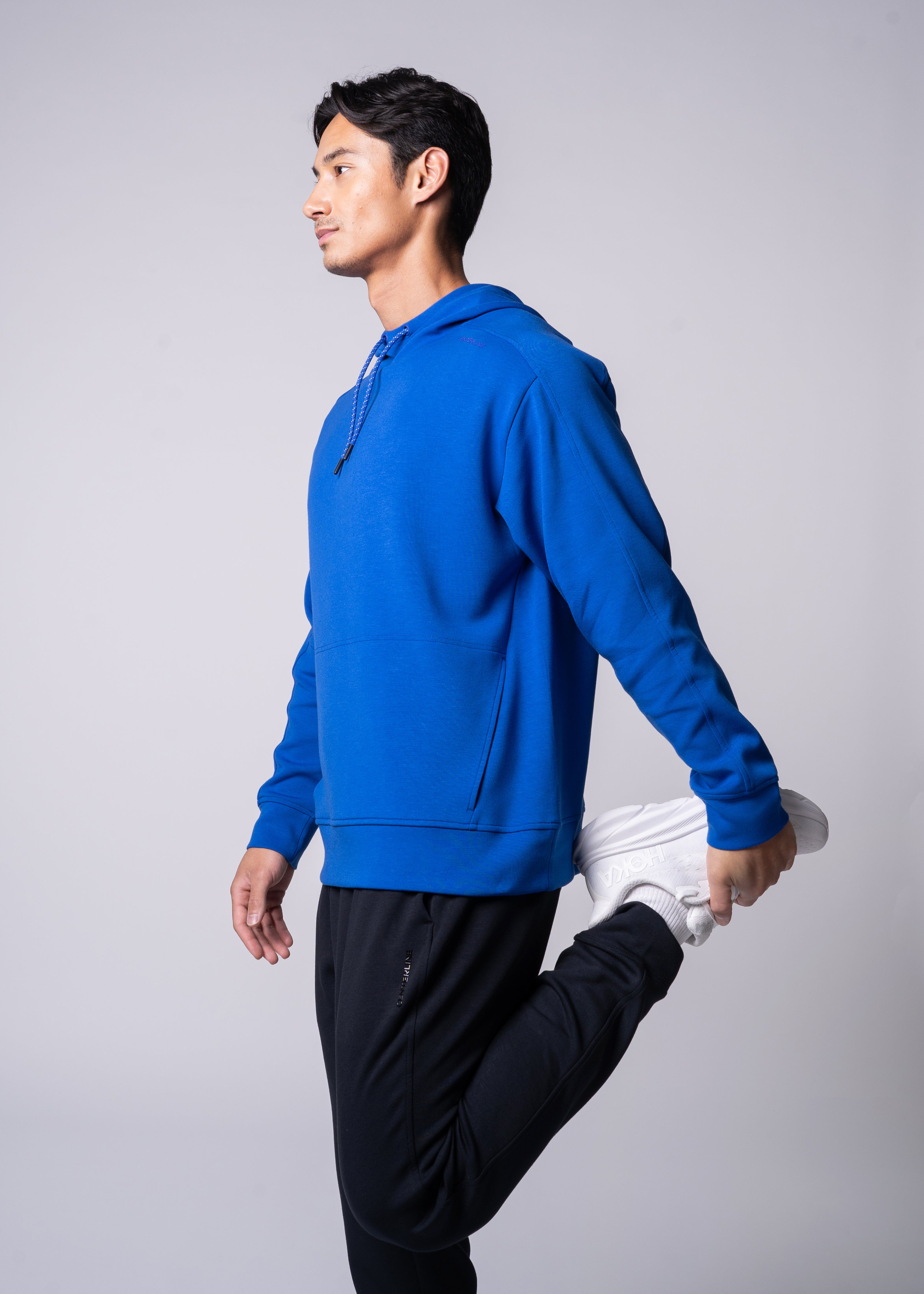 Man in blue hoodie stretching with white sneakers.