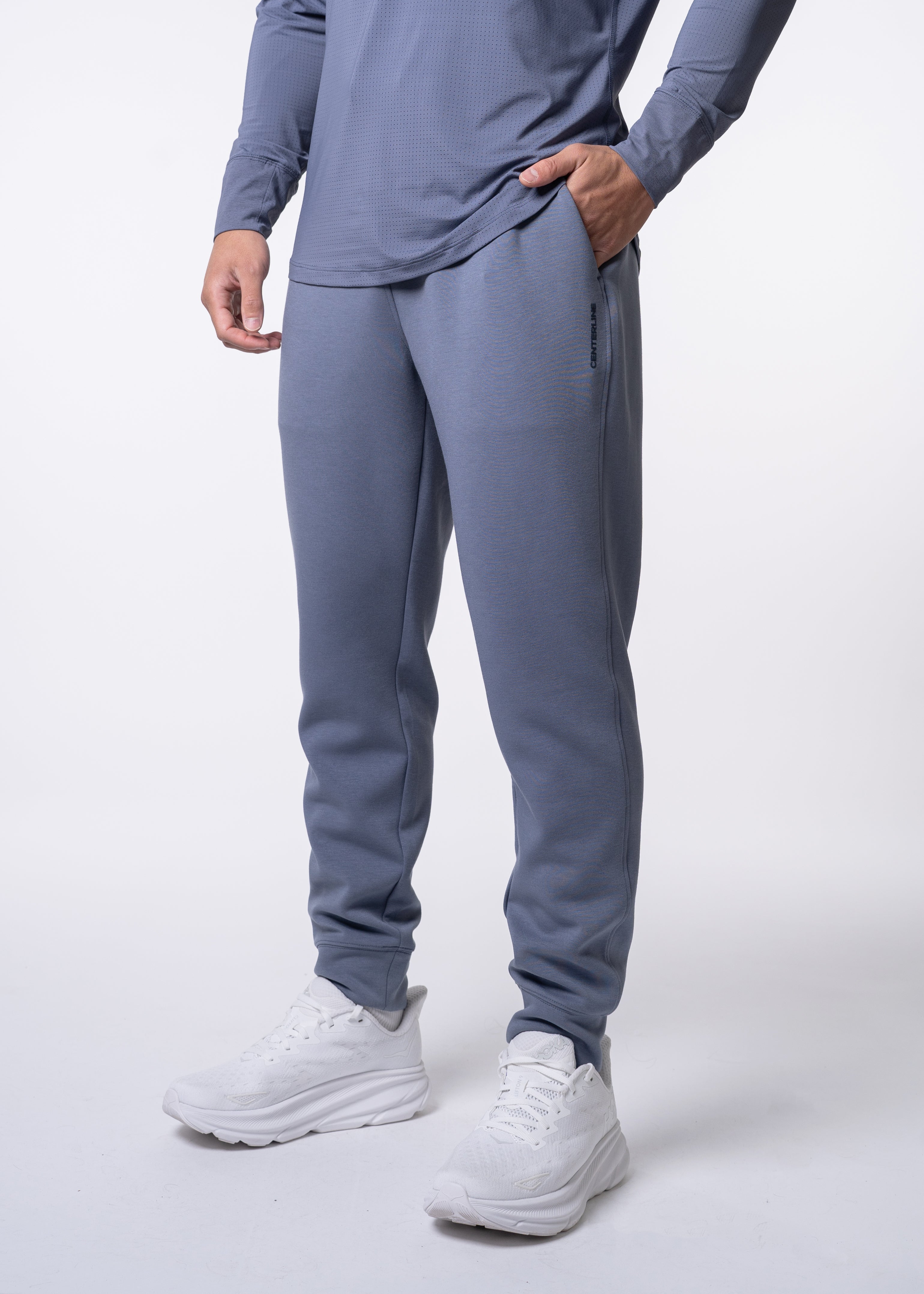 Blue-grey men's jogger pants by Centerline Athletics, featuring vertical 'CENTERLINE' text, worn with a matching perforated long-sleeve top and white athletic shoes.