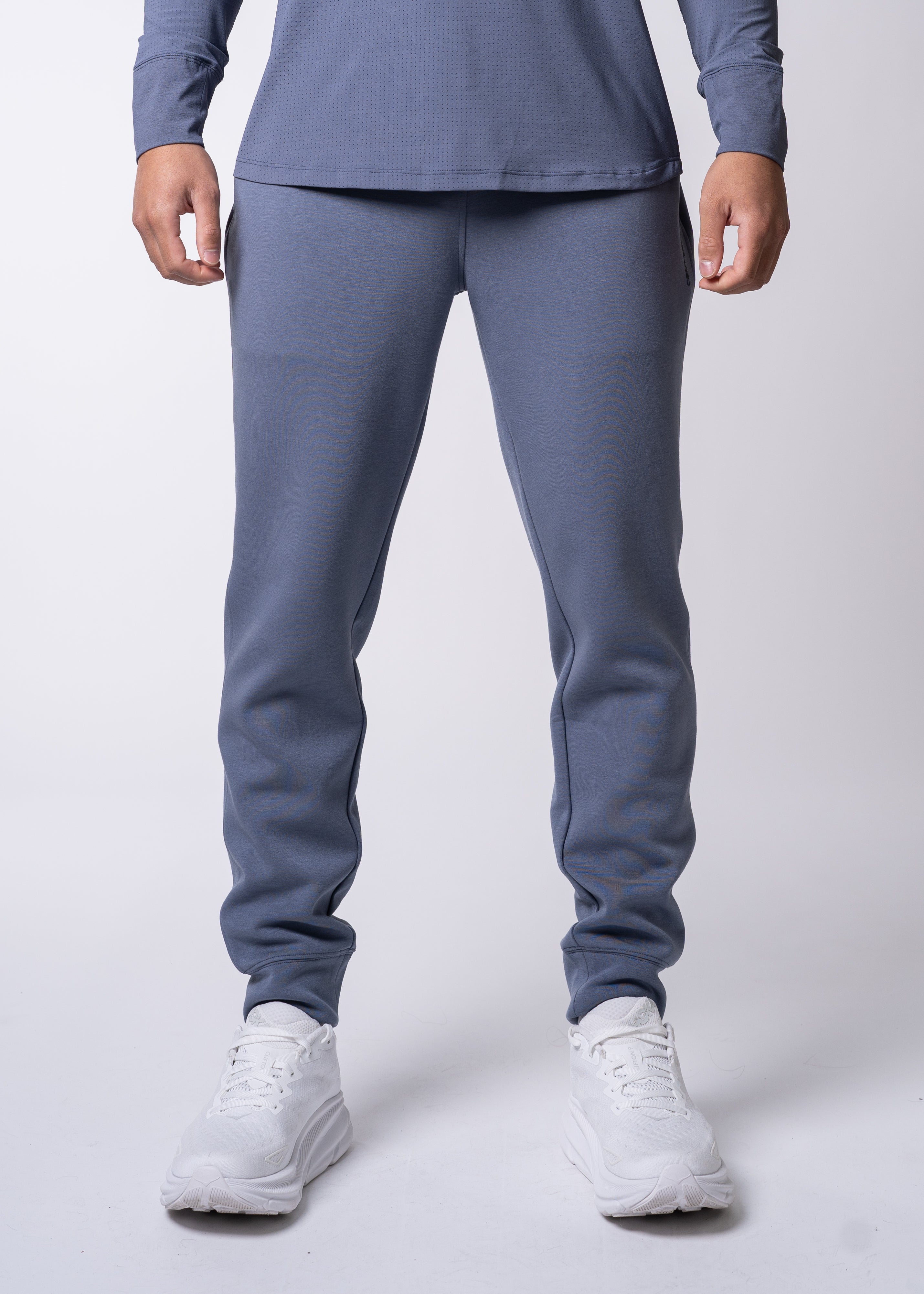 Men's heathered blue-grey Après Jogger by Centerline Athletics, featuring a tapered leg and ribbed cuffs, worn with a matching long-sleeve top and white athletic shoes.