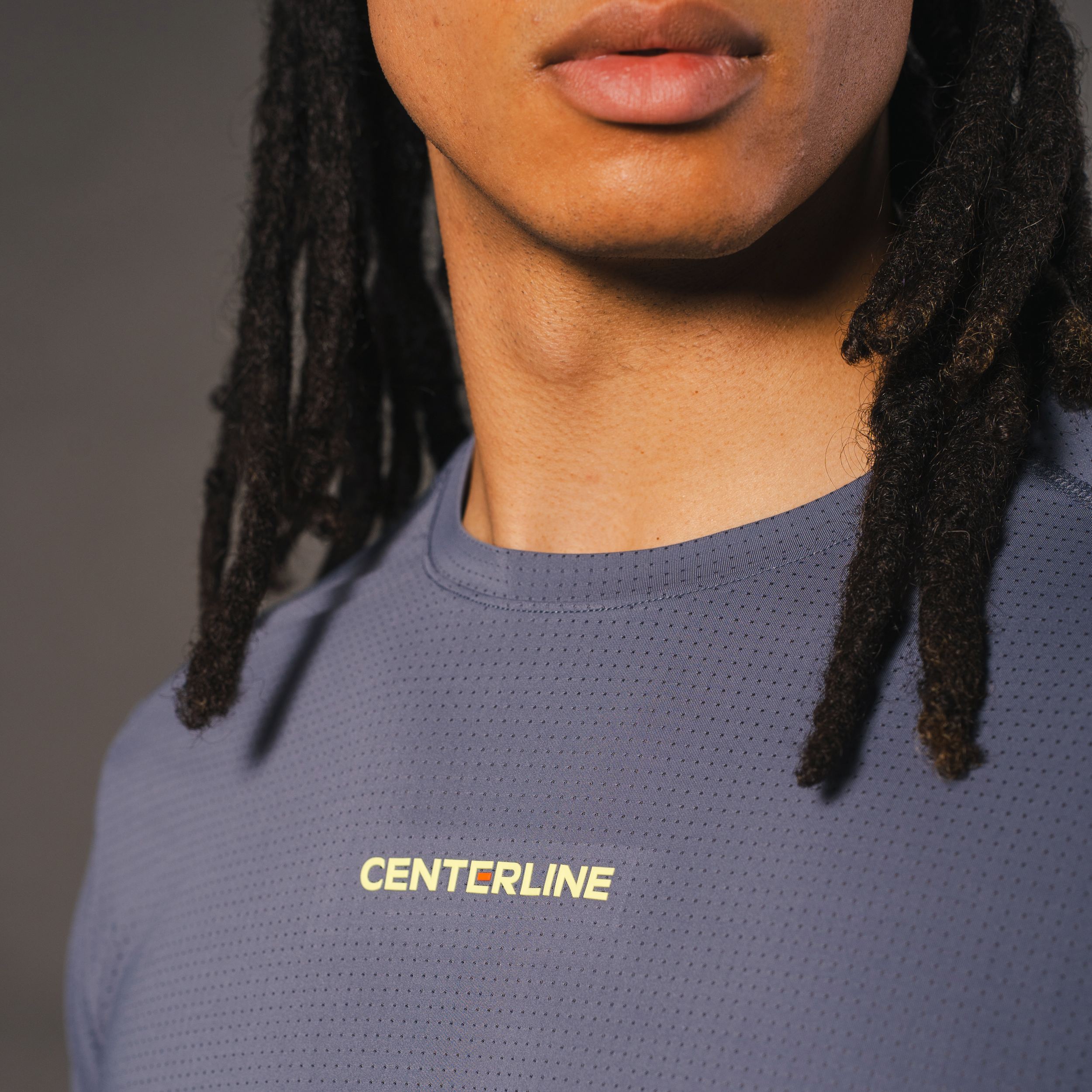 Close-up of a person with dreadlocks wearing a blue perforated athletic shirt with the word "CENTERLINE" in yellow.