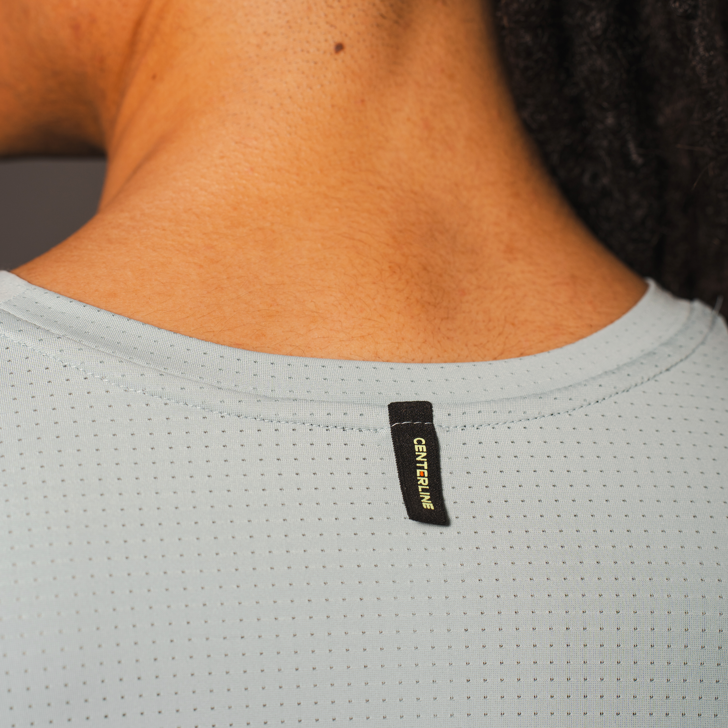 Close up of person's neck and shoulders, wearing a pale blue athletic shirt with small perforated holes and a black centerline tag.